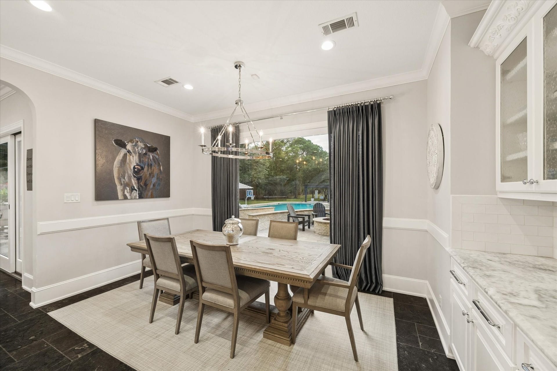 Spacious breakfast area featuring a butler's pantry and glass-front cabinetry. Large seamless windows provide an expansive view of the backyard, pool, and fire pit.