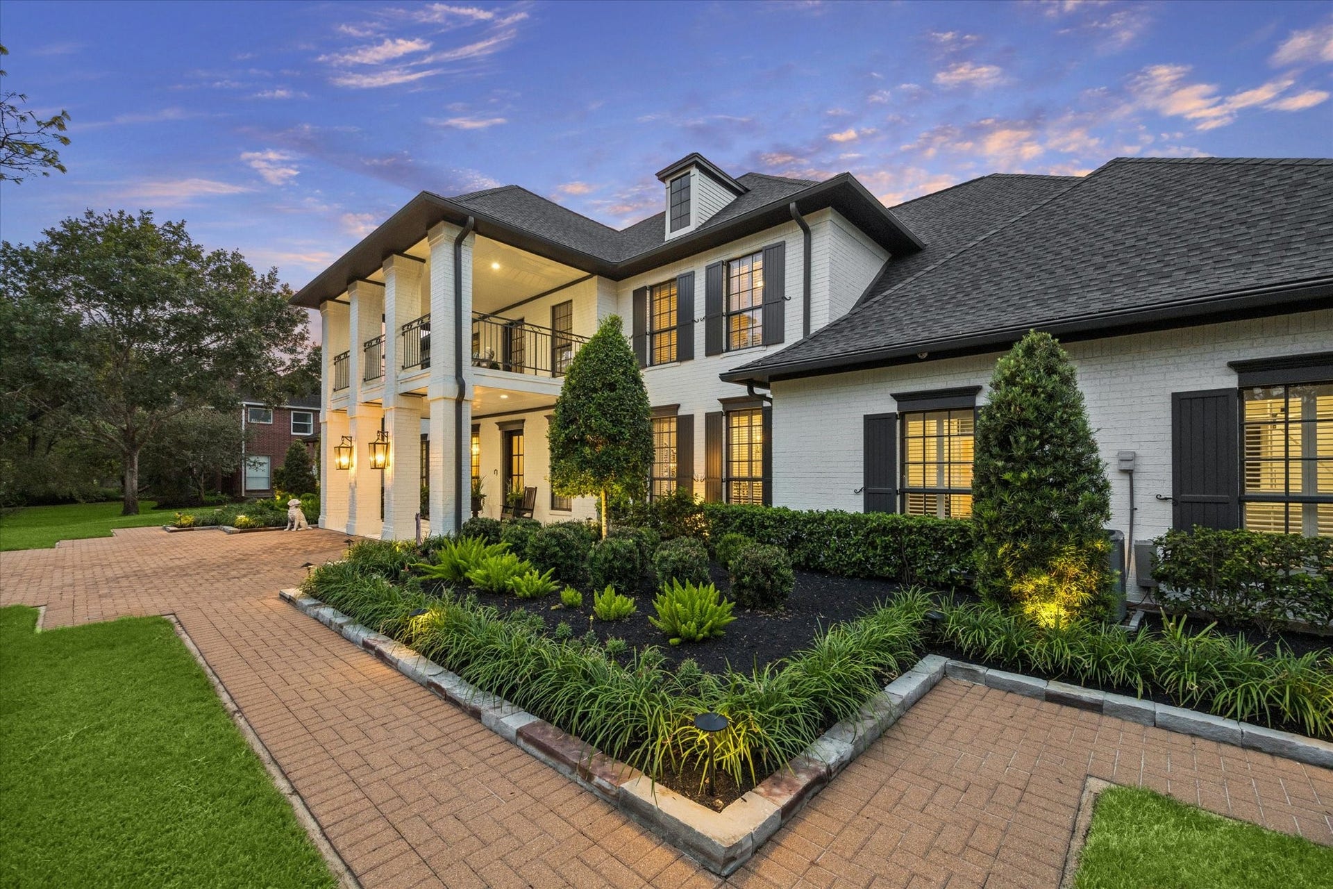 Stunning two-story home featuring elegant columns, a beautifully landscaped front yard, and a spacious brick driveway.