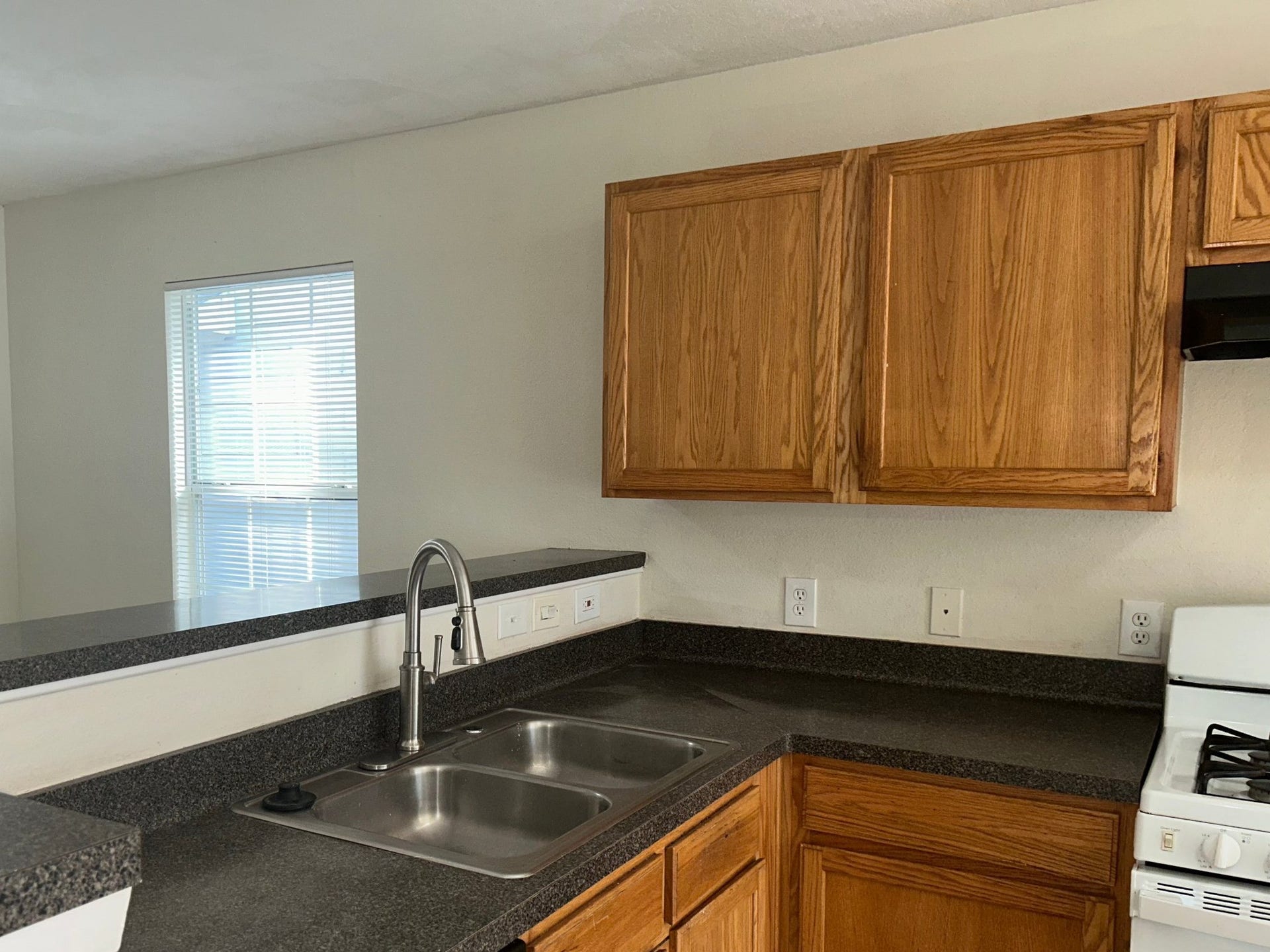 Kitchen with oak cabinets, dark countertops, a double stainless sink with a pull-down faucet, a gas range, and a raised breakfast bar.