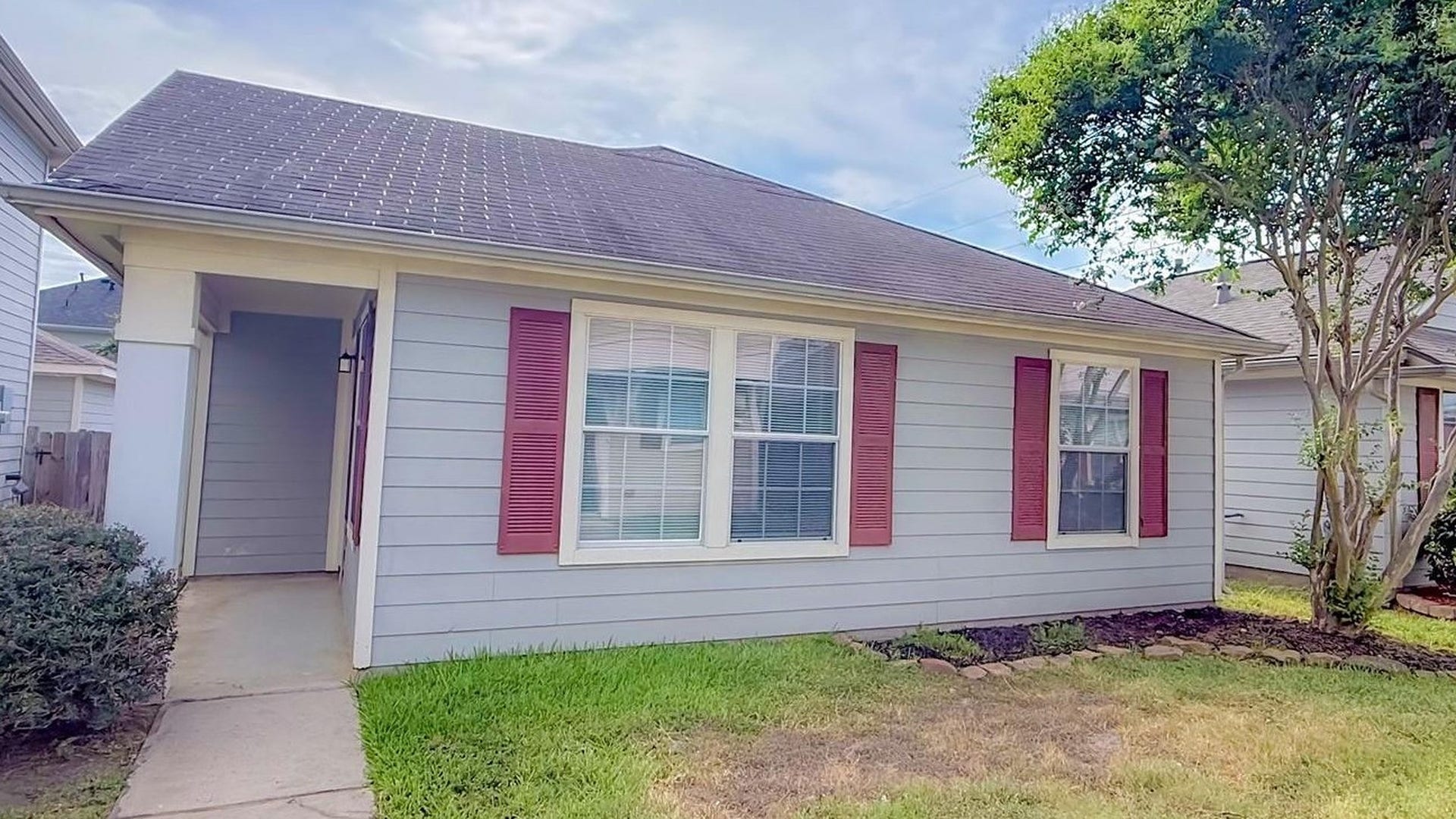 Welcome home to a charming house with light gray siding, classic red shutters, a covered entry and a stone edge flower bed