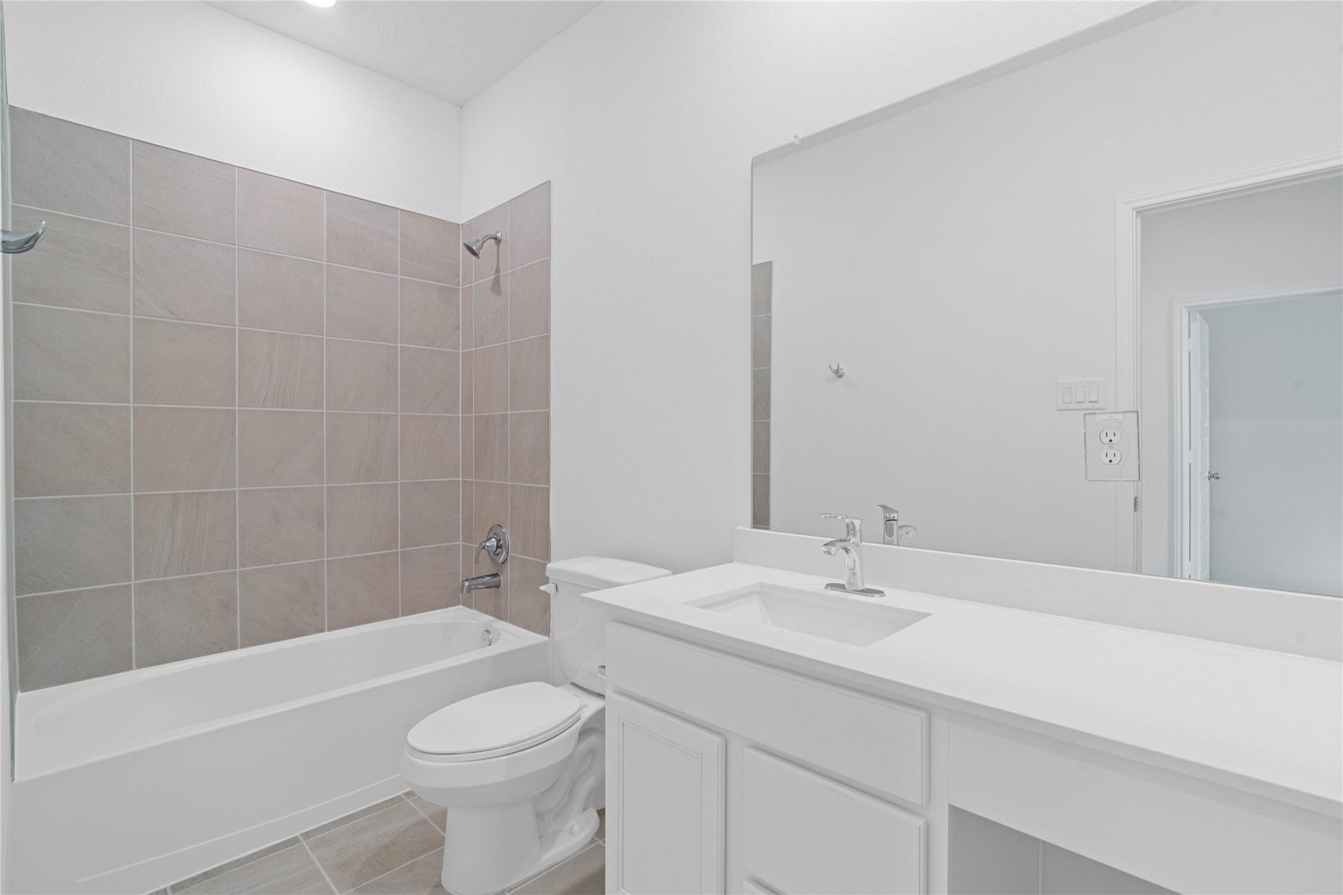 The secondary bathroom showcases tile flooring, a bath/shower combo with Daltile tile surround, a vanity with knee space and stunning light countertop, a mirror, sleek fixtures, and contemporary finishes throughout.