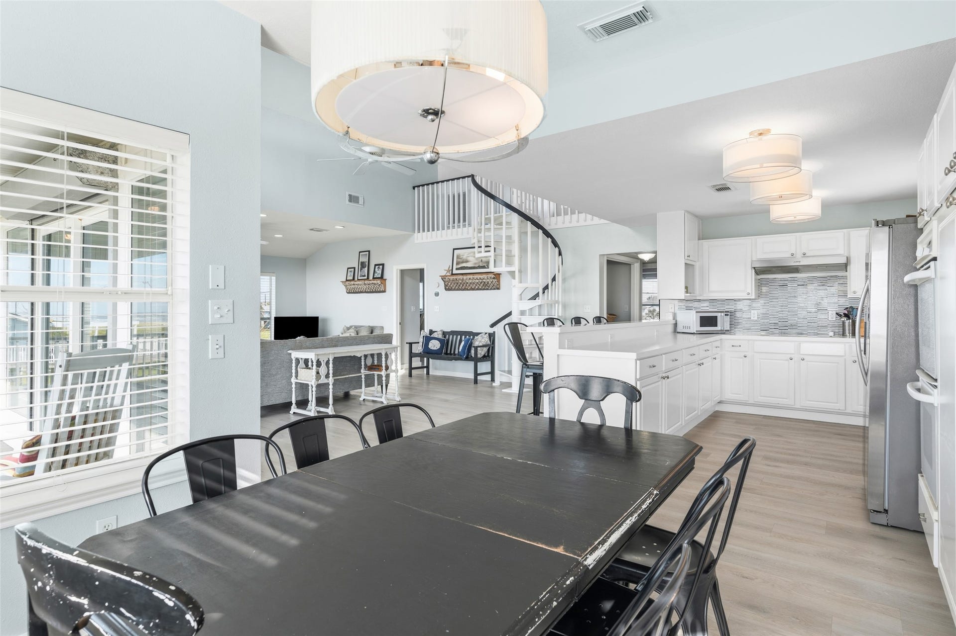 21631 Termini San Luis Pass Road, Galveston, TX 77554 Open living space featuring a modern kitchen with coastal white cabinetry, a cozy dining area, and a stylish spiral staircase.
