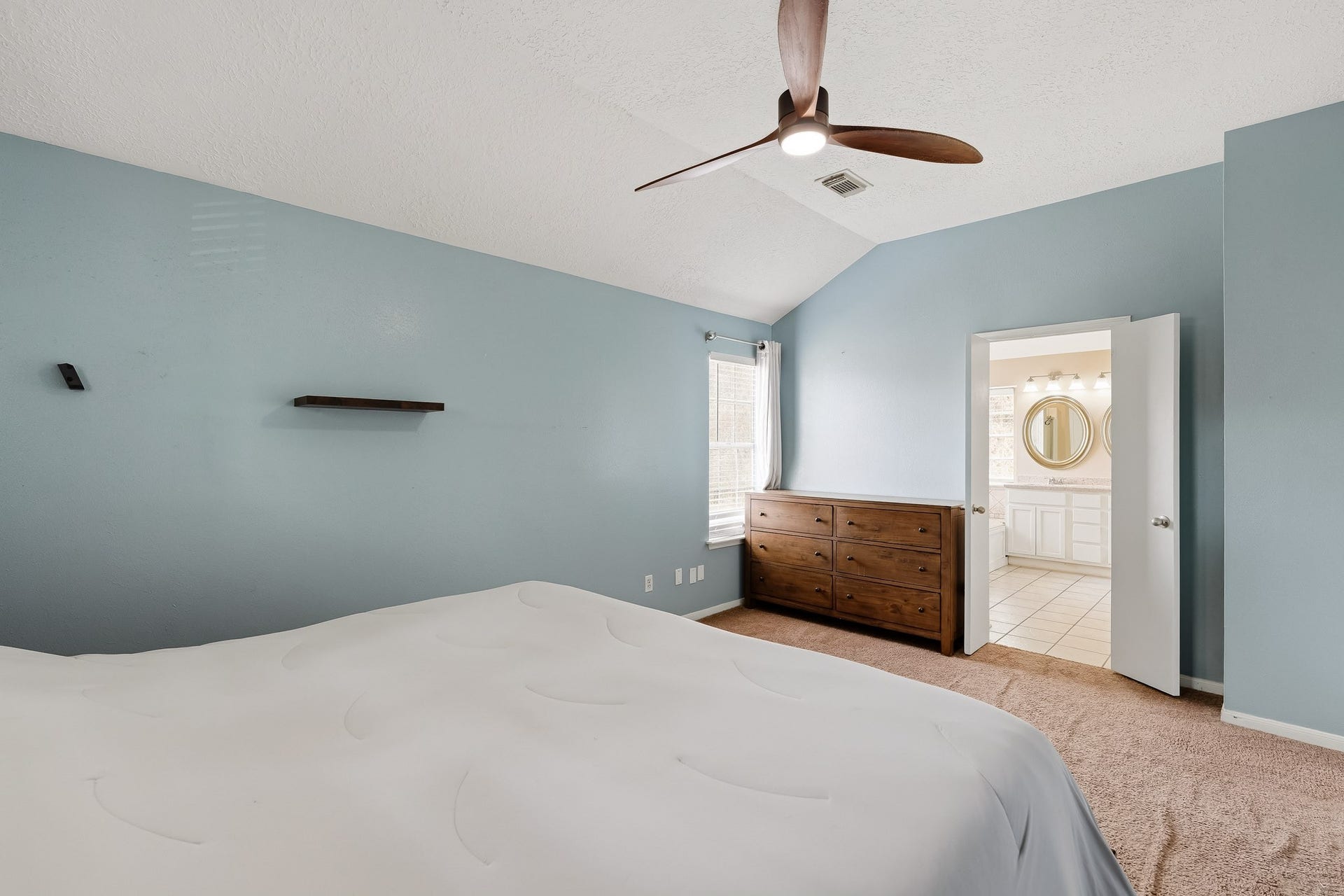 4811 Red Lantern Drive, Friendswood, TX 77546 Spacious bedroom with soothing blue walls, featuring a ceiling fan, cozy carpeting, and an ensuite bathroom for added convenience.