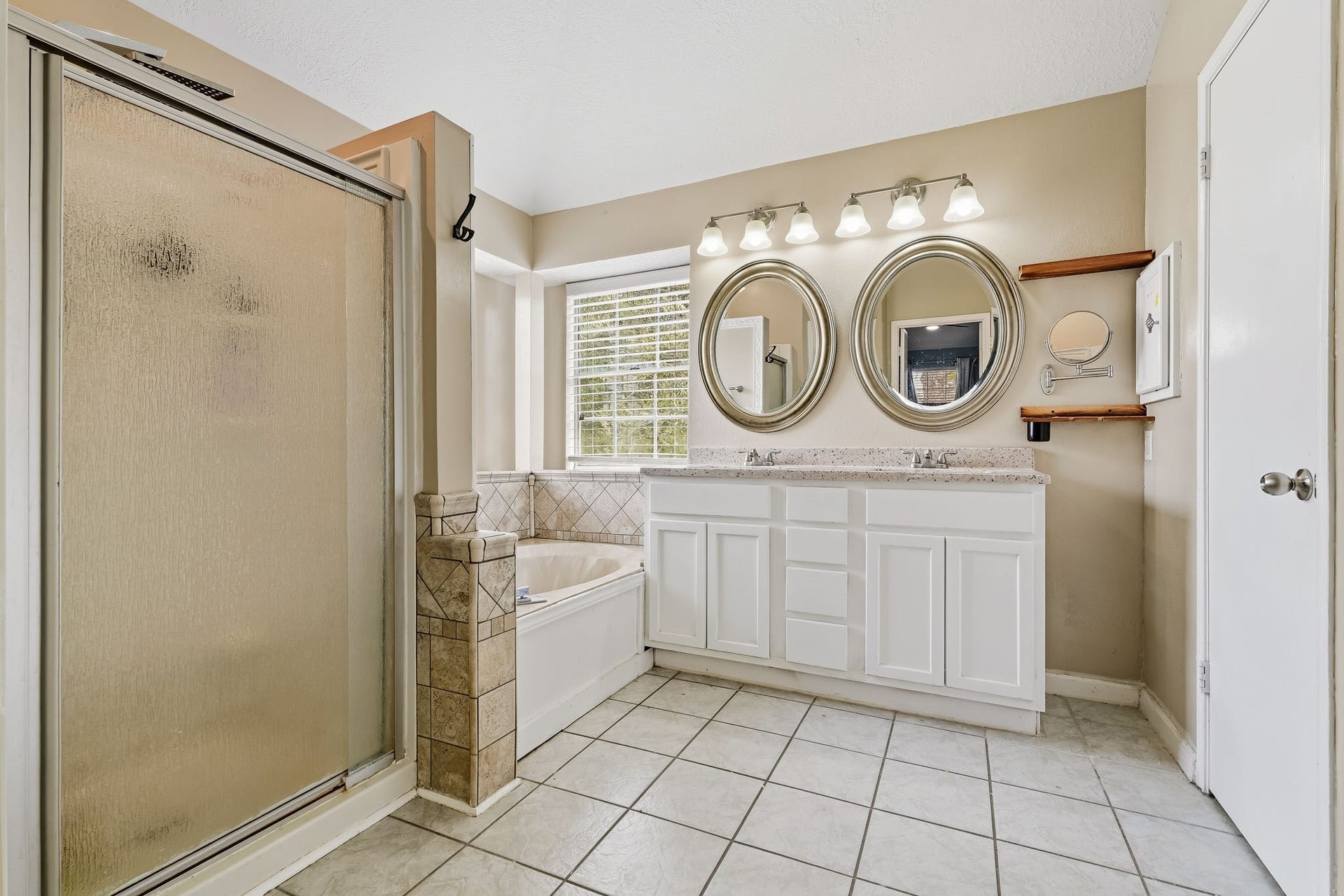 4811 Red Lantern Drive, Friendswood, TX 77546 Spacious bathroom with a large walk-in shower, elegant dual vanity with round mirrors, and a cozy jetted tub under a bright window.