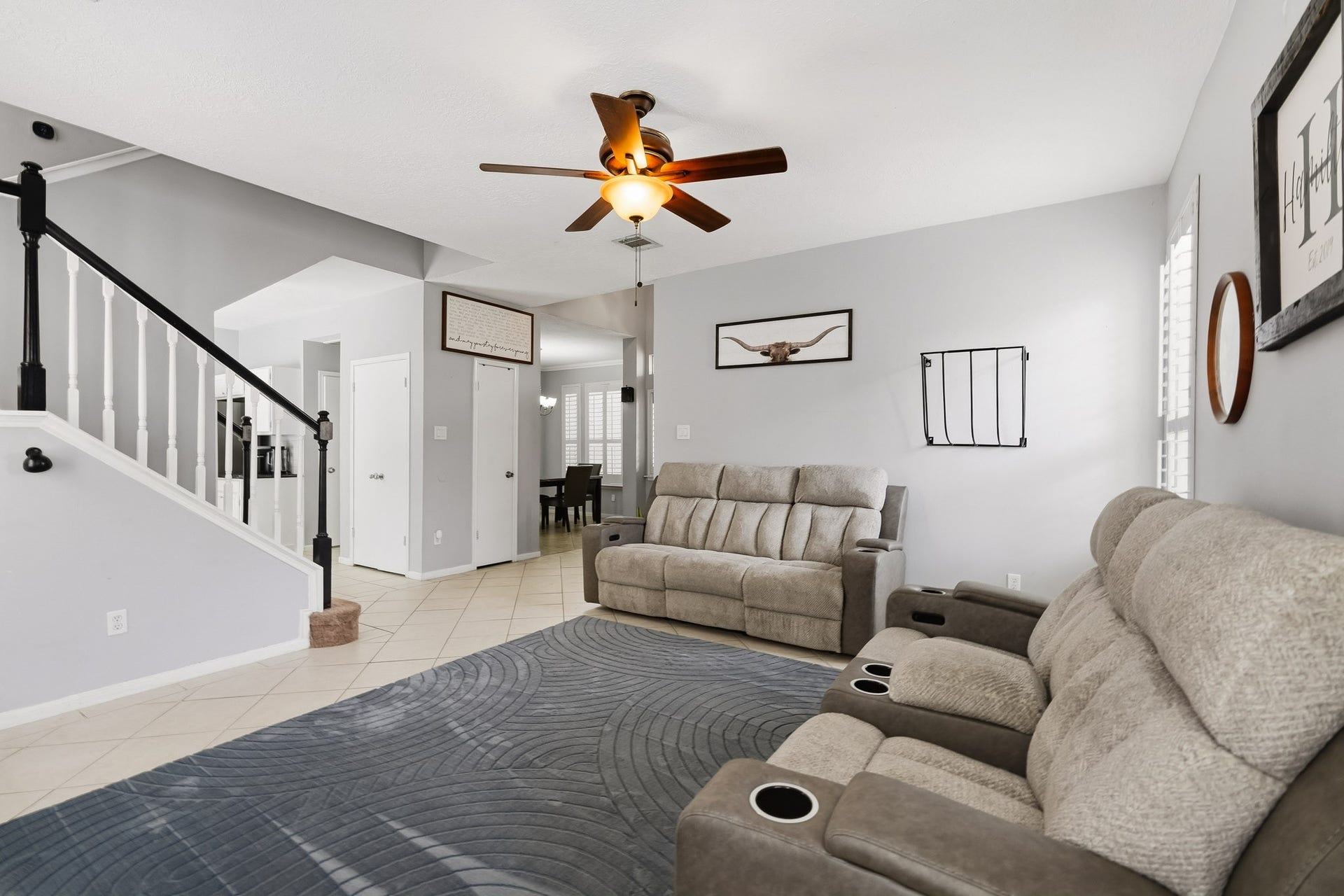 4811 Red Lantern Drive, Friendswood, TX 77546 Spacious living room with a stylish ceiling fan and modern tile flooring. An elegant staircase and open layout lead to the dining area and kitchen, creating a welcoming atmosphere.