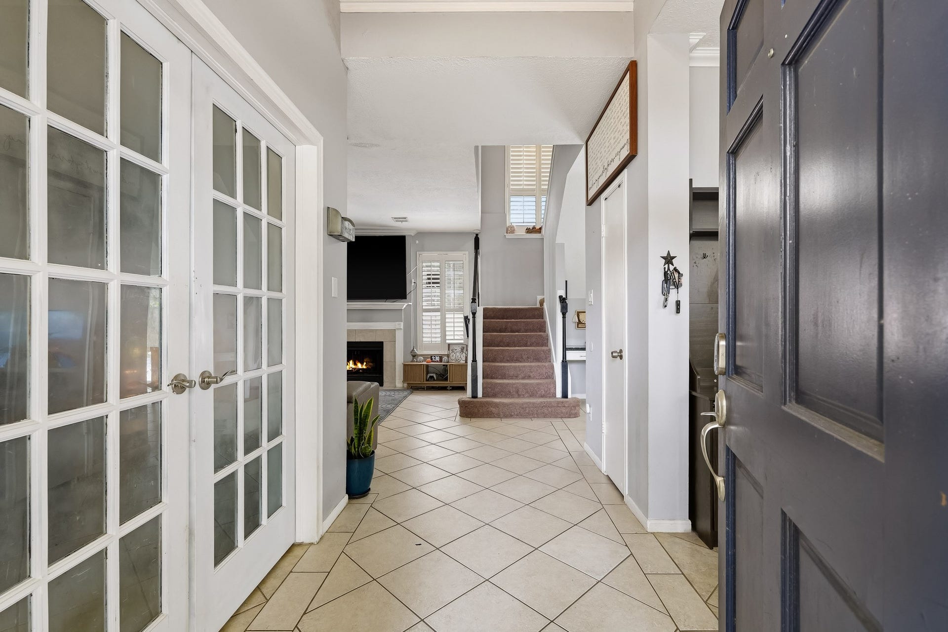 4811 Red Lantern Drive, Friendswood, TX 77546 Inviting entryway with elegant French doors, leading to a cozy living area featuring a fireplace and a staircase, offering a warm and welcoming atmosphere.