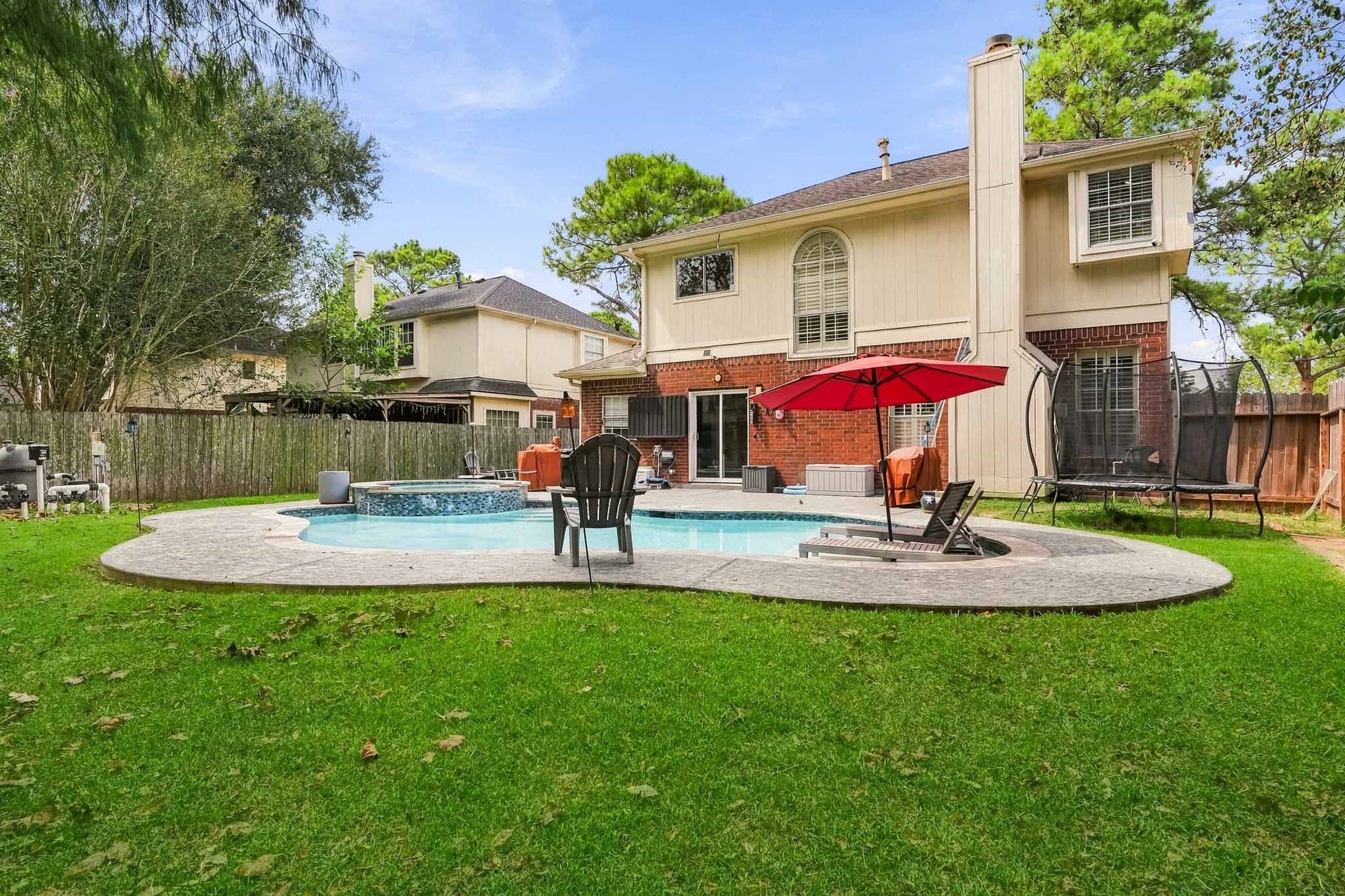 4811 Red Lantern Drive, Friendswood, TX 77546 Inviting backyard retreat featuring a sparkling pool with a spa, surrounded by lush greenery and ample patio space for outdoor entertaining.