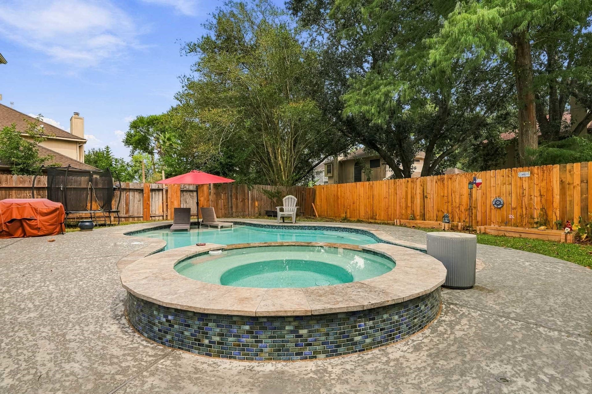4811 Red Lantern Drive, Friendswood, TX 77546 Charming backyard oasis featuring a sparkling pool and spa, surrounded by lush greenery and a privacy fence, perfect for relaxation and entertaining.