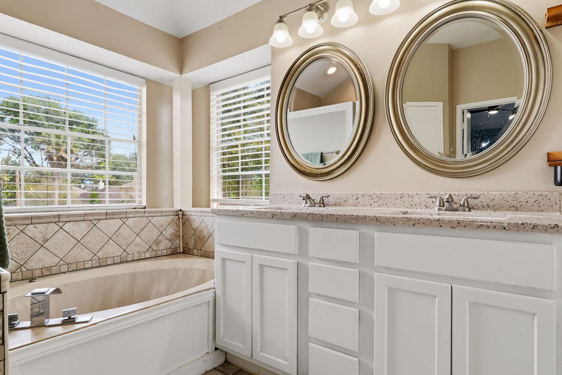 4811 Red Lantern Drive, Friendswood, TX 77546 Bright and inviting bathroom with dual sinks, elegant round mirrors, and a luxurious corner bathtub surrounded by large windows for natural light.