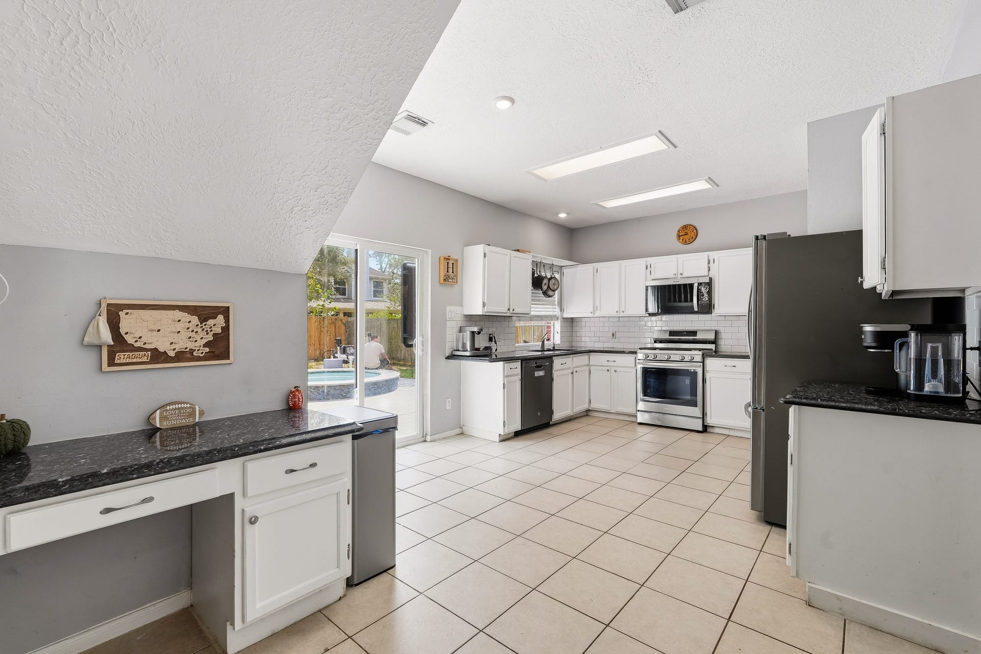 4811 Red Lantern Drive, Friendswood, TX 77546 Spacious kitchen with modern appliances, ample counter space, and a convenient desk area, featuring a bright, open view to the backyard pool through large sliding doors.
