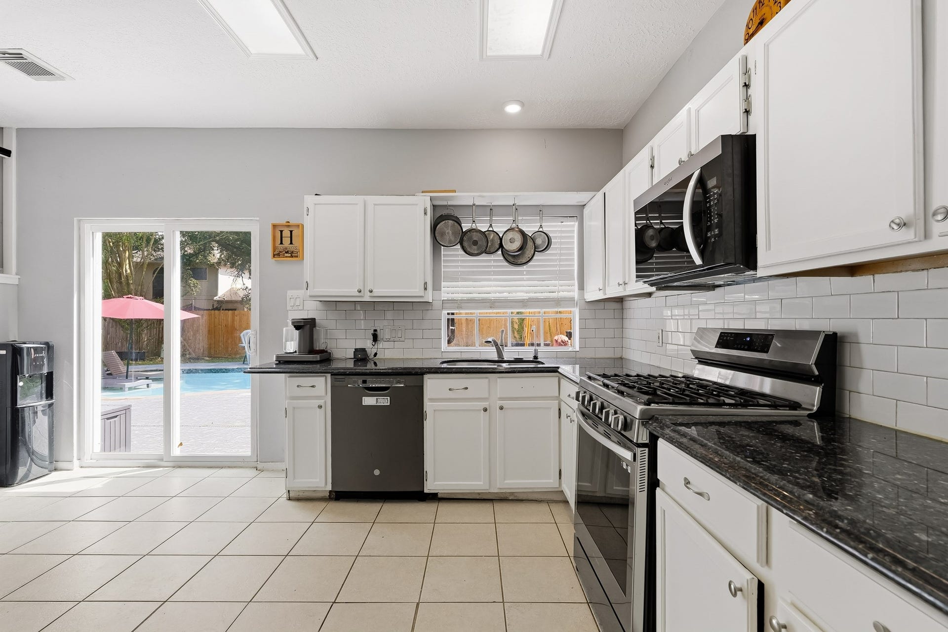 4811 Red Lantern Drive, Friendswood, TX 77546 Bright kitchen with sleek black countertops, modern appliances, and ample cabinet space. Large windows offer a view of the inviting pool area, enhancing the open, airy feel.