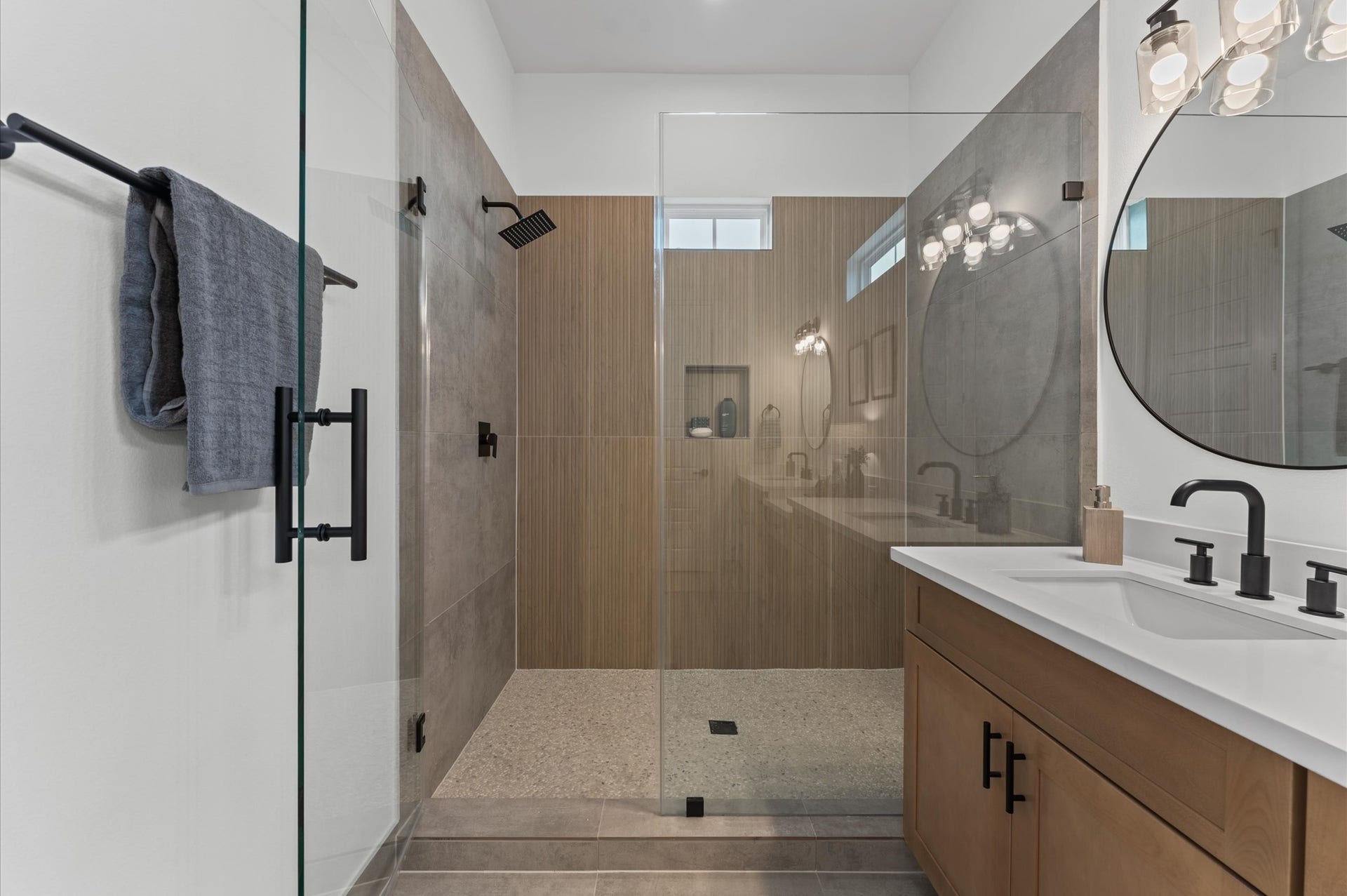 This stylish primary bathroom showcases a spacious walk-in shower framed with sleek glass panels and modern tilework that adds texture and sophistication. A double sink vanity anchors the space with clean lines and ample countertop room, complemented by an abundance of cabinetry that offers both function and flair. Contemporary finishes tie the room together, creating a polished retreat that balances luxury with everyday practicality.