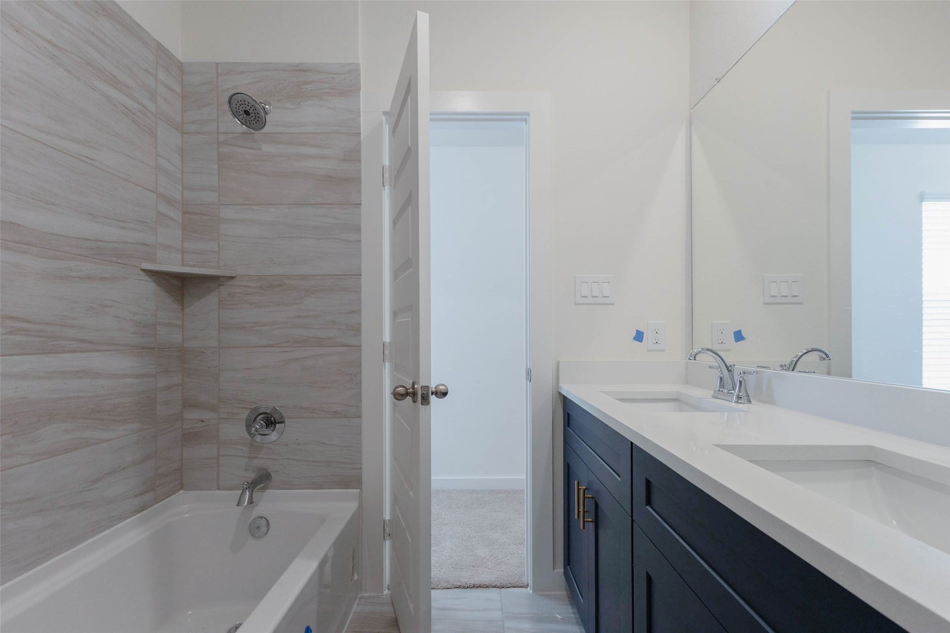 1115 Santee Court, Rosharon, TX 77583 A closer look at the shared bath shows a tub-shower wrapped in wood-grain tile with a built-in corner shelf for toiletries. Next to it, the double-sink vanity offers lots of drawer and cabinet space, and a doorway leads straight to the hall for easy access from the bedrooms. It is a clean, stylish bathroom designed to handle busy mornings.