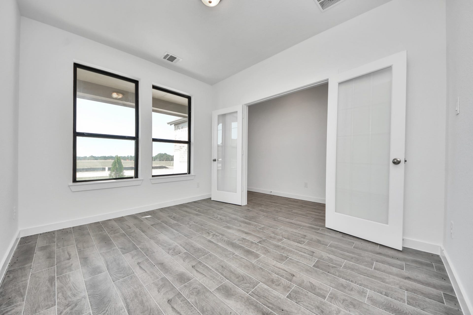 1017 Golden Glow Path, Magnolia, TX 77355 Experience the perfect blend of sophistication and warmth in this home office, boasting elegant wood-look tile flooring and flooded with natural light from expansive windows and French doors.