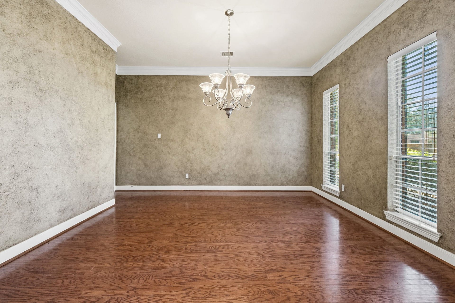 7514 Water Wood Trail, Kingwood, TX 77346 Elegant dining room with rich hardwood floors, textured walls, and a stylish chandelier. Large windows provide ample natural light, creating a warm and inviting atmosphere.