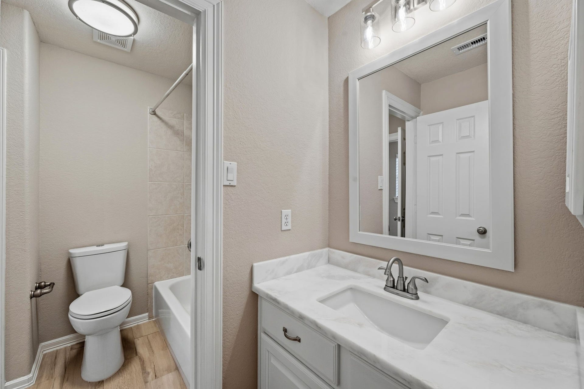 7514 Water Wood Trail, Kingwood, TX 77346 Charming bathroom featuring a sleek vanity, modern lighting, and a classic tub-shower combination, all complemented by warm wood-look flooring.