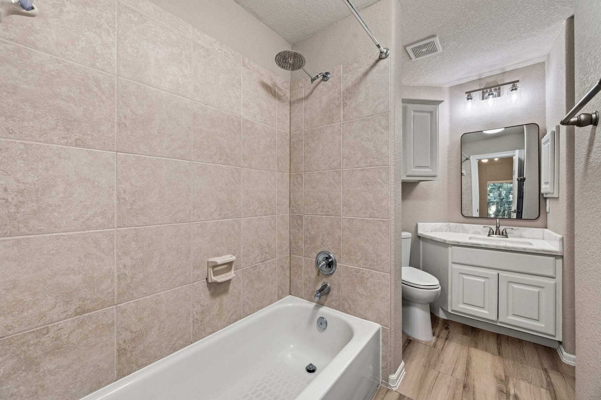 7514 Water Wood Trail, Kingwood, TX 77346 Modern bathroom featuring a tiled shower and bathtub combo, elegant vanity with ample storage, and contemporary fixtures, complemented by warm wood-style flooring.