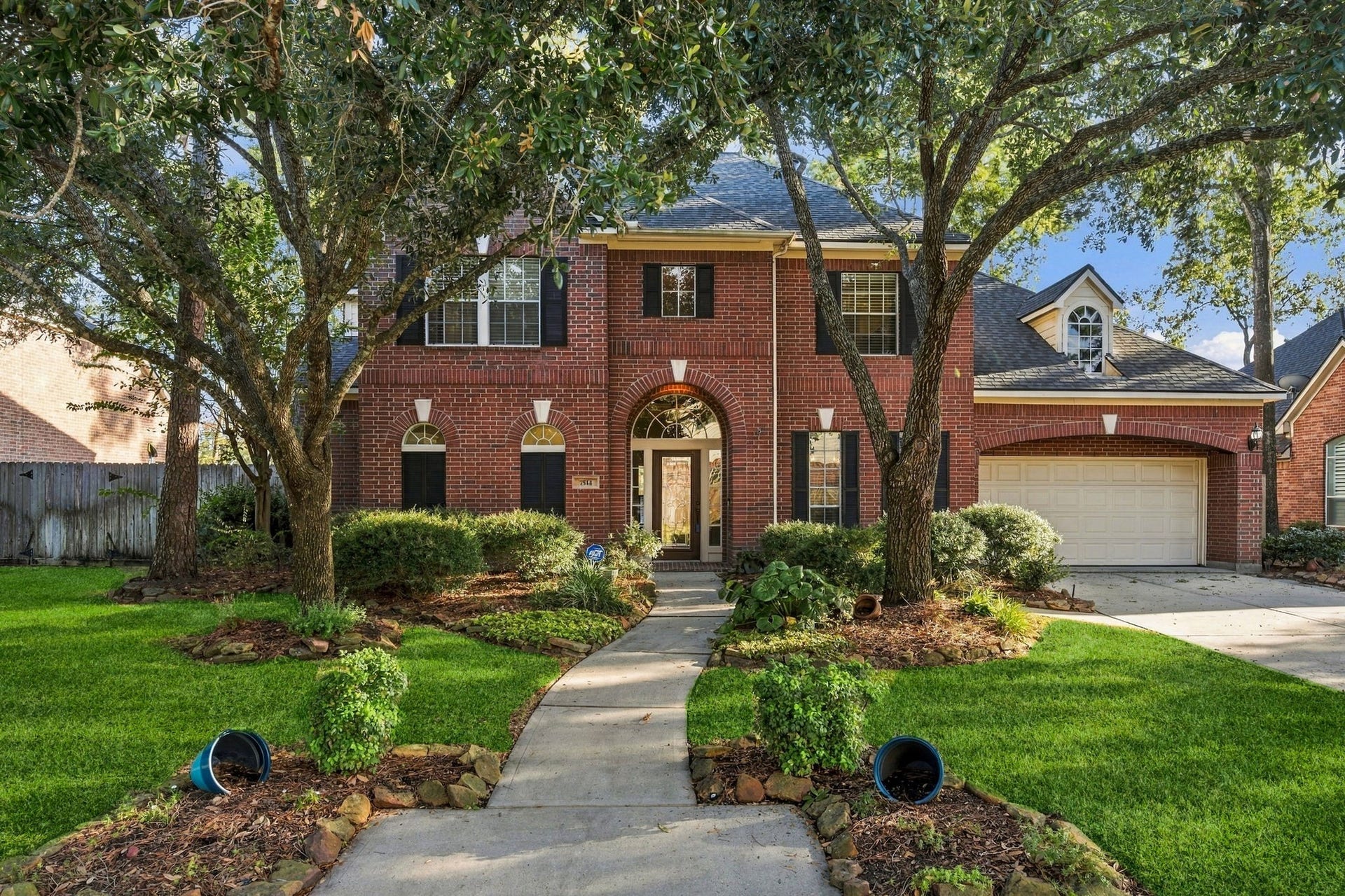 7514 Water Wood Trail, Kingwood, TX 77346 Stately brick home with charming arched windows and a welcoming front path, nestled among mature trees and lush landscaping.