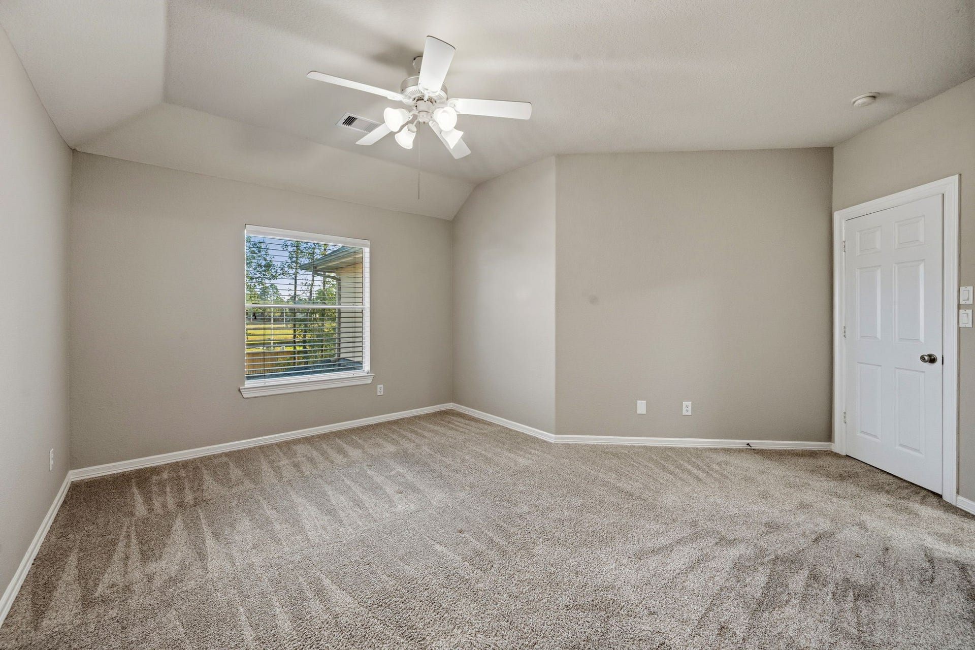 7514 Water Wood Trail, Kingwood, TX 77346 Spacious bedroom with plush carpeting, neutral walls, and ample natural light from a large window, complemented by a ceiling fan for comfort.