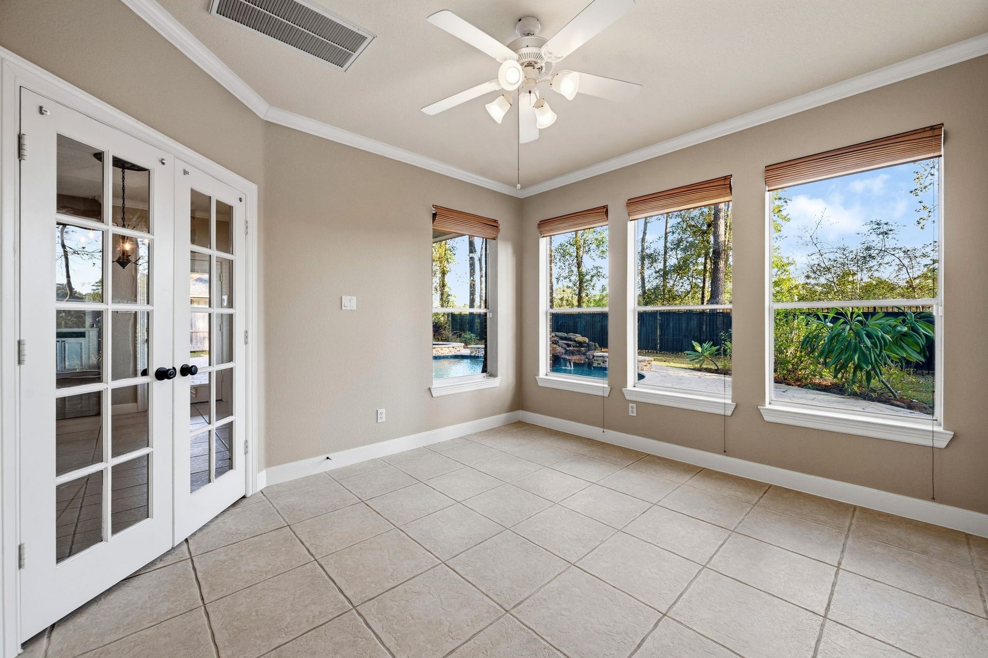 7514 Water Wood Trail, Kingwood, TX 77346 Bright sunroom with tile flooring, ceiling fan, and large windows offering serene views of the backyard and pool. French doors add elegance and connect to the rest of the home.