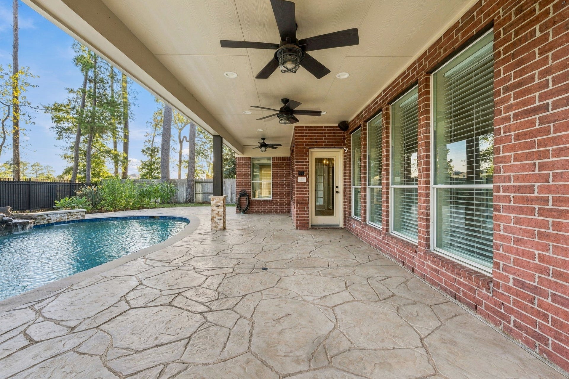 7514 Water Wood Trail, Kingwood, TX 77346 Spacious covered patio with elegant stone flooring and ceiling fans, overlooking a sparkling pool set amid a serene backdrop.