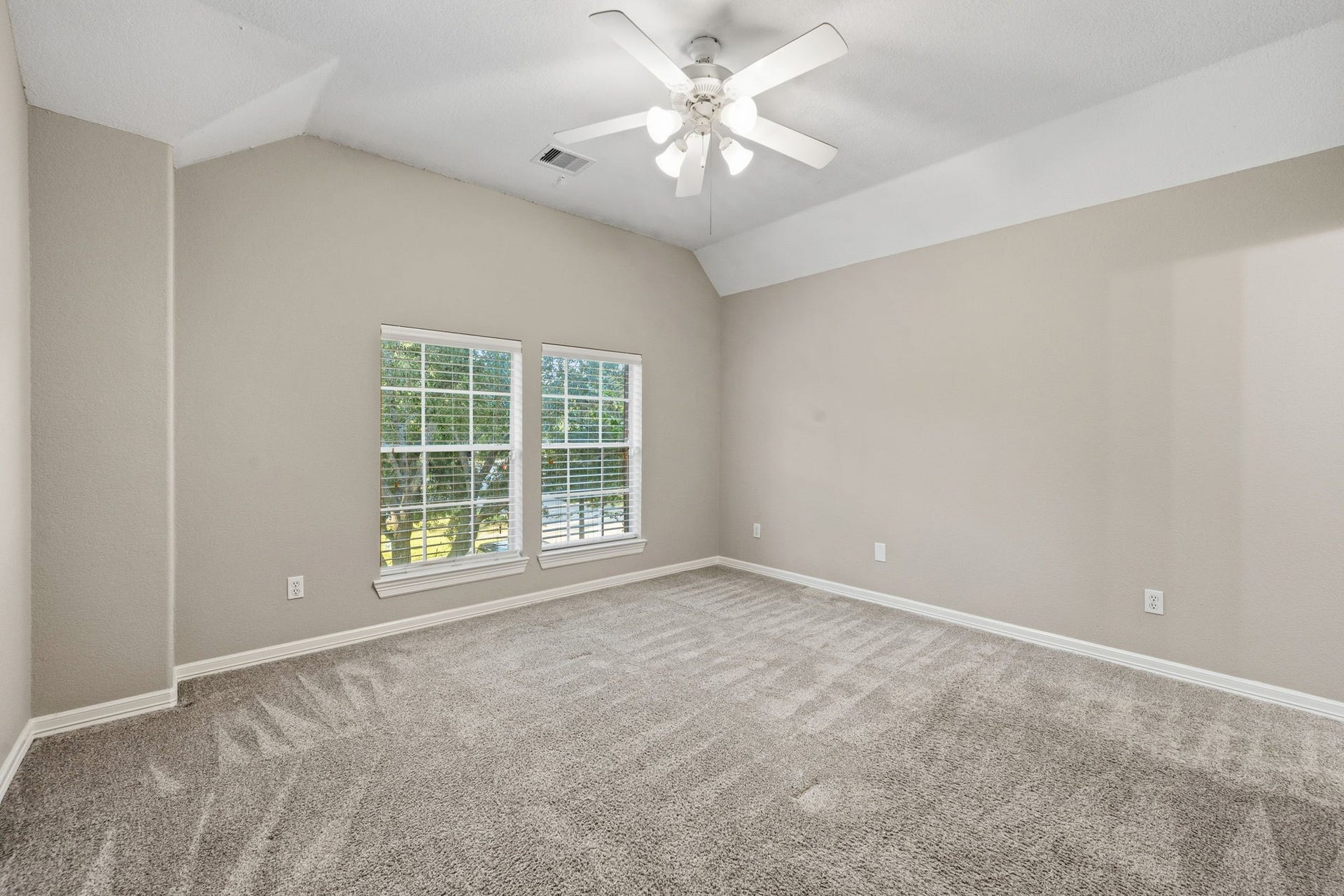 7514 Water Wood Trail, Kingwood, TX 77346 Spacious and bright bedroom with neutral walls, plush carpeting, and large windows letting in natural light, complemented by a ceiling fan for added comfort.
