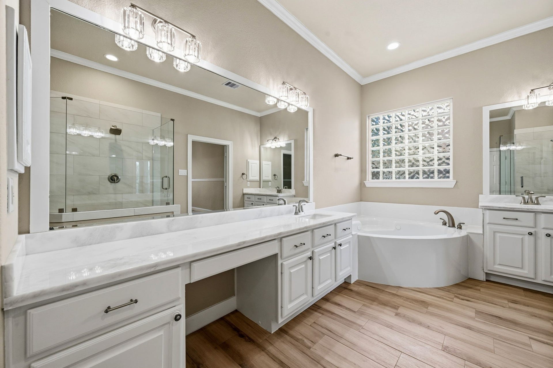 7514 Water Wood Trail, Kingwood, TX 77346 Elegant bathroom featuring a spacious vanity with dual sinks, a luxurious soaking tub, and a glass-enclosed shower, all accented by chic lighting and warm wood-like flooring.