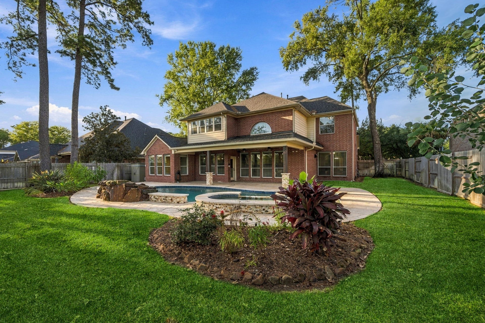 7514 Water Wood Trail, Kingwood, TX 77346 Spacious backyard featuring a sparkling pool, lush landscaping, and a charming brick home with large windows and a covered patio, perfect for outdoor entertaining.
