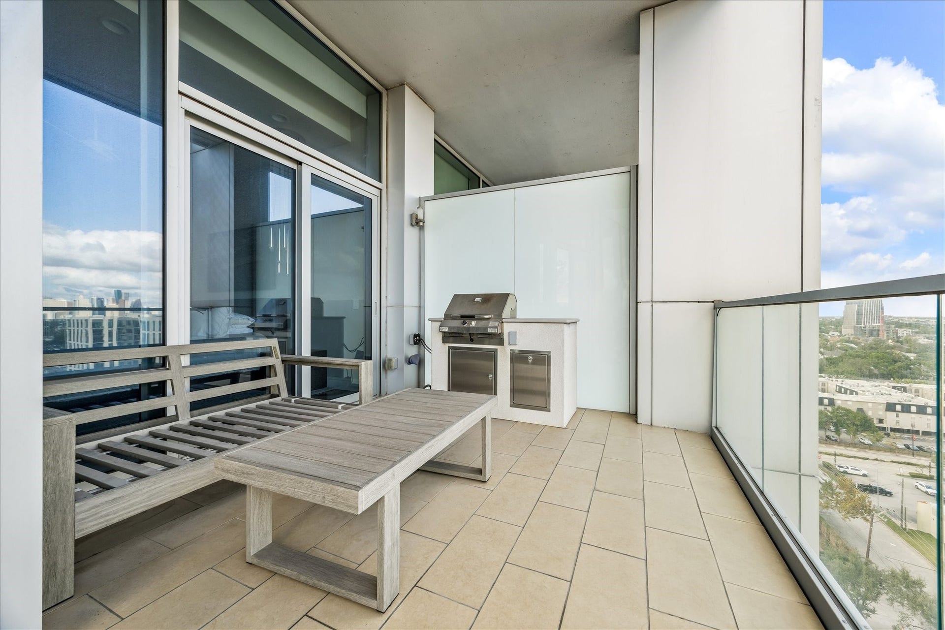 Covered terrace with tile flooring, built-in grill station, and glass railing overlooking the city.