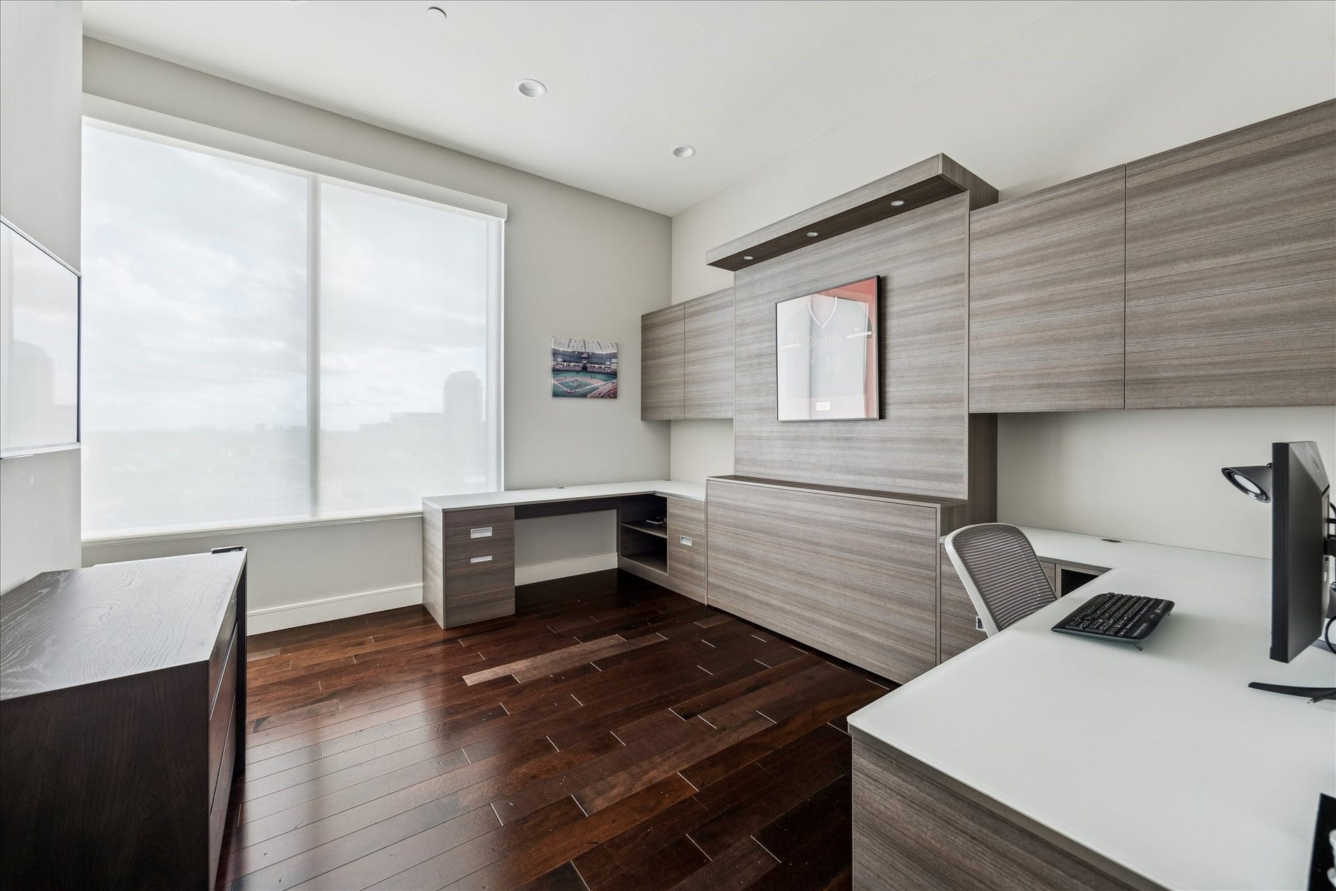 Flexible room with custom built-in cabinetry, large window with natural light, hardwood floors, and recessed lighting.