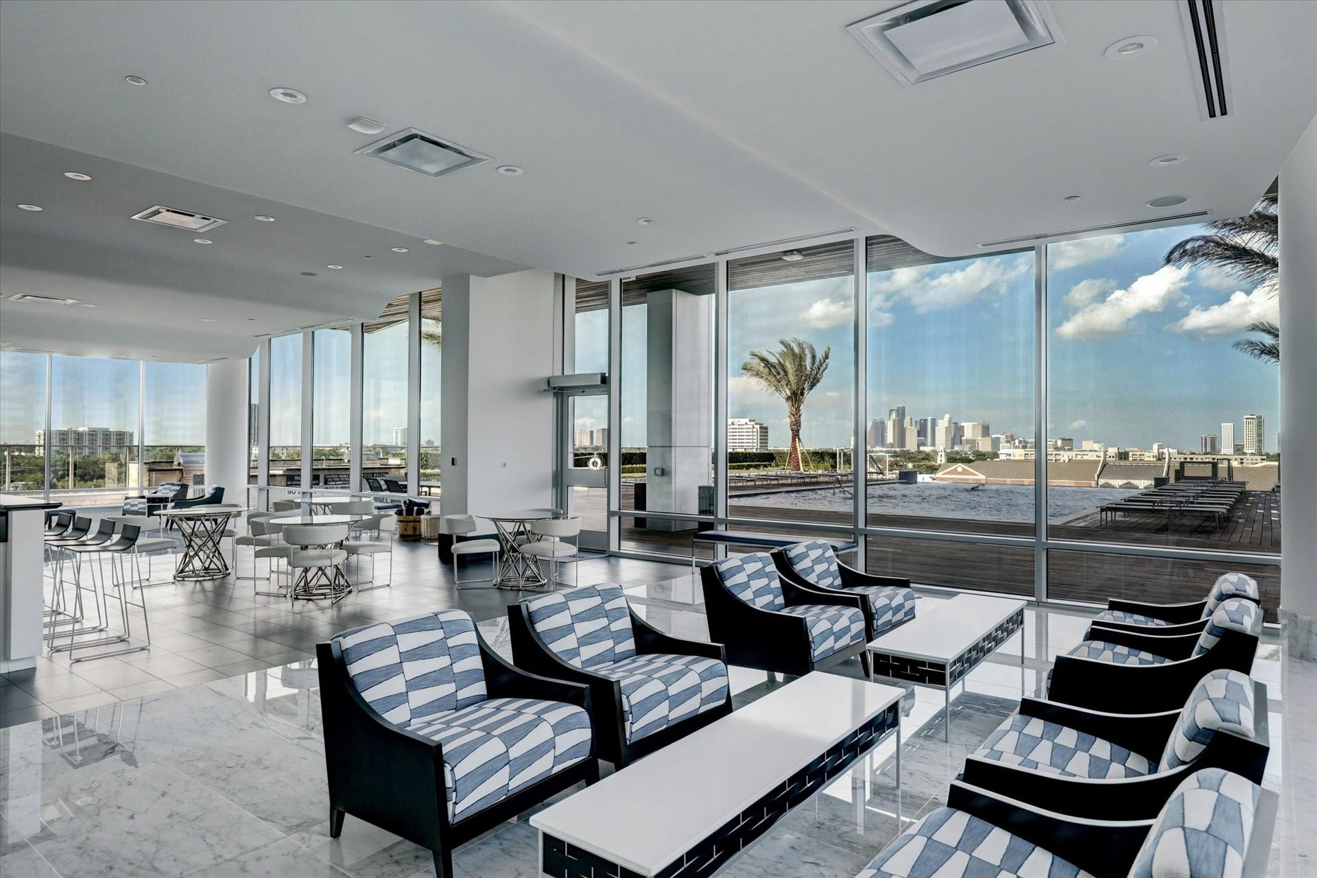 Resident lounge and entertaining space with floor-to-ceiling windows, tile flooring, and access to outdoor terrace with city views.