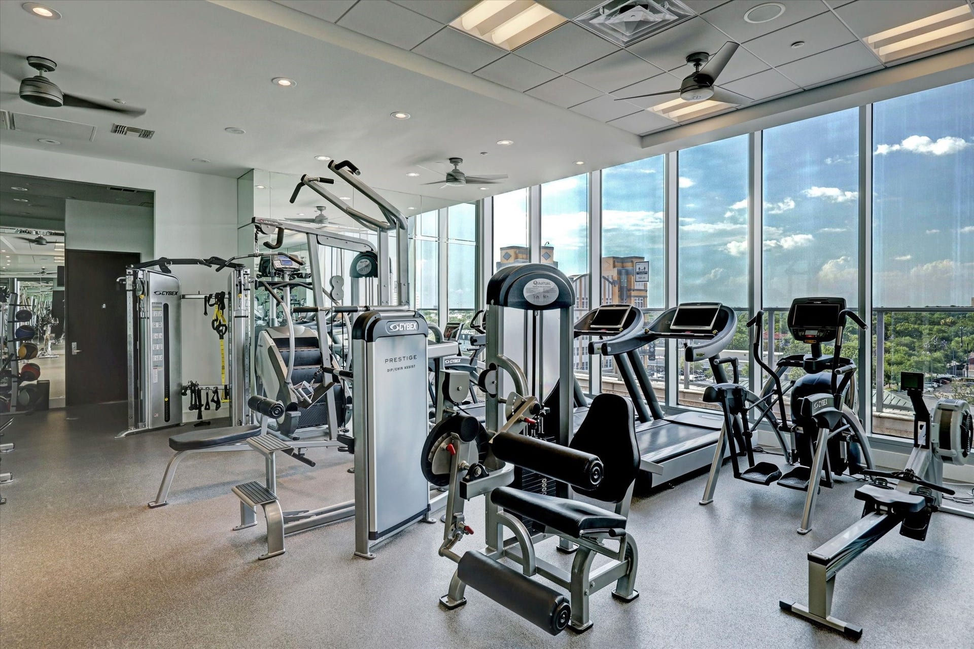 Fully equipped fitness center with cardio and strength equipment, floor-to-ceiling windows, and panoramic skyline views.
