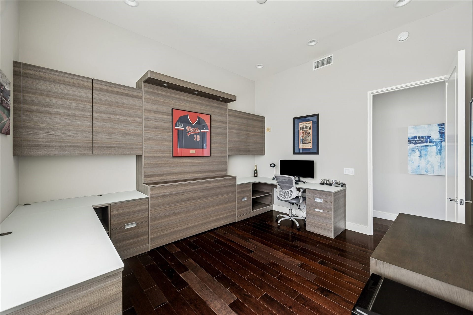 Shows custom wall-to-wall cabinetry with integrated storage, workspace surface, recessed lighting, and hardwood flooring.
