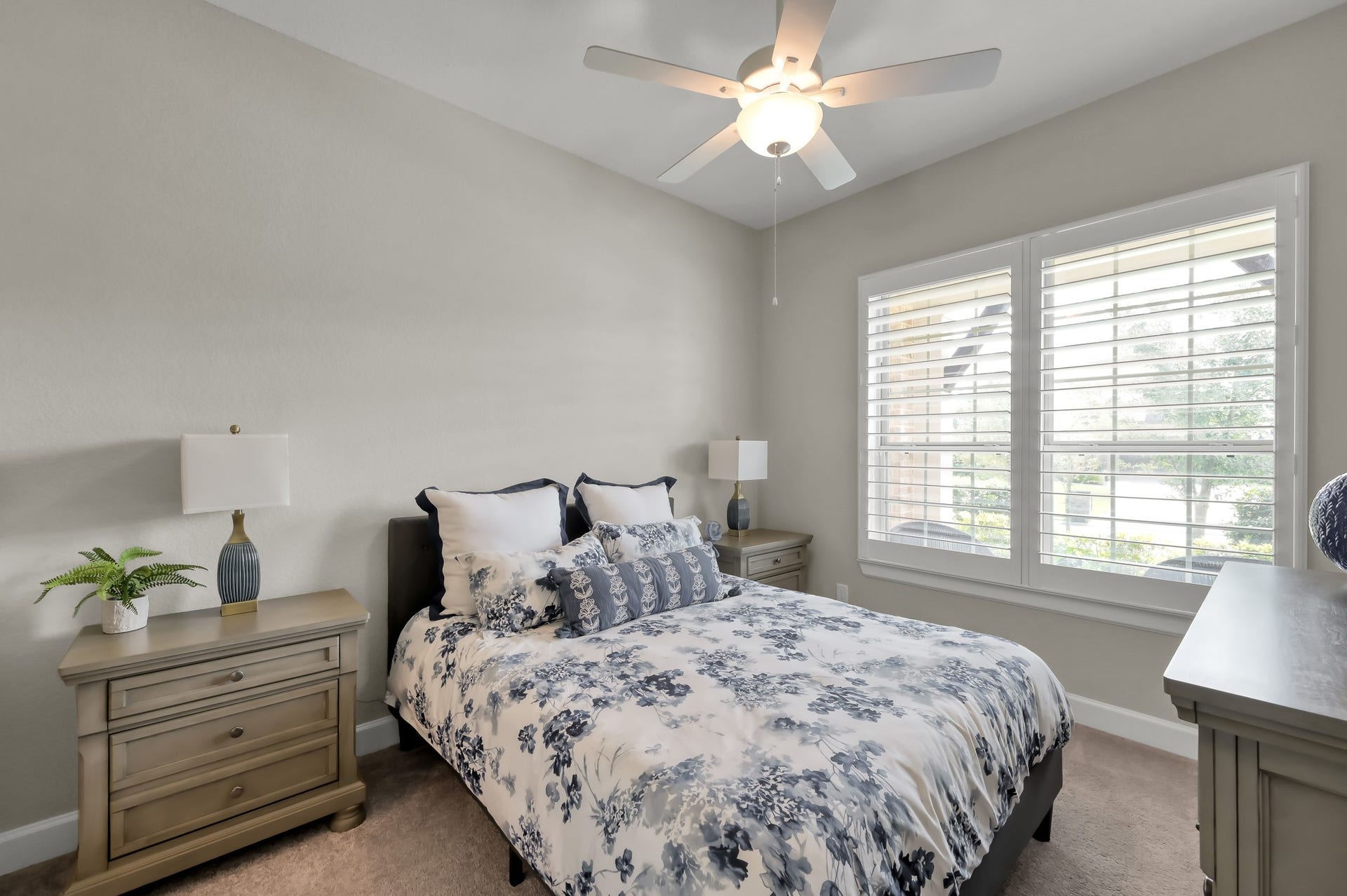Bright secondary bedroom with plantation shutters, soft natural light, and cozy, neutral finishes.