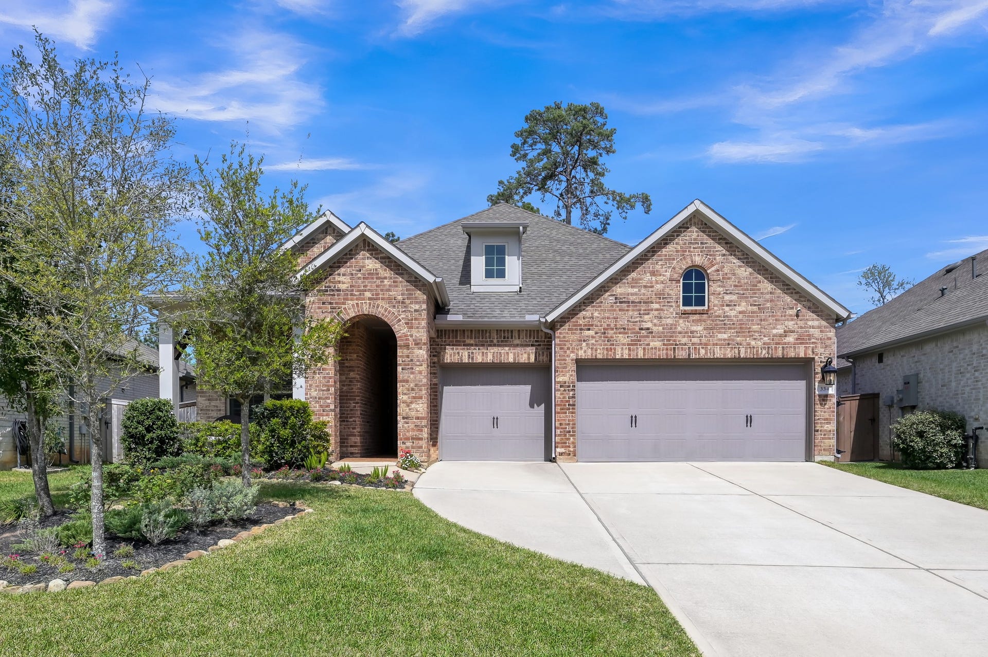 David Weekley 1.5-story home built in 2021 featuring beautiful brick elevation, inviting arched entry, and exceptional curb appeal with a spacious 3-car garage.