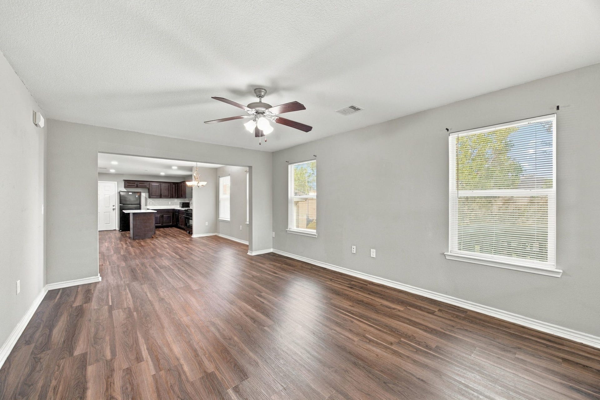 Spacious living area featuring wood-look flooring, neutral walls, a ceiling fan, and an open connection to the kitchen.