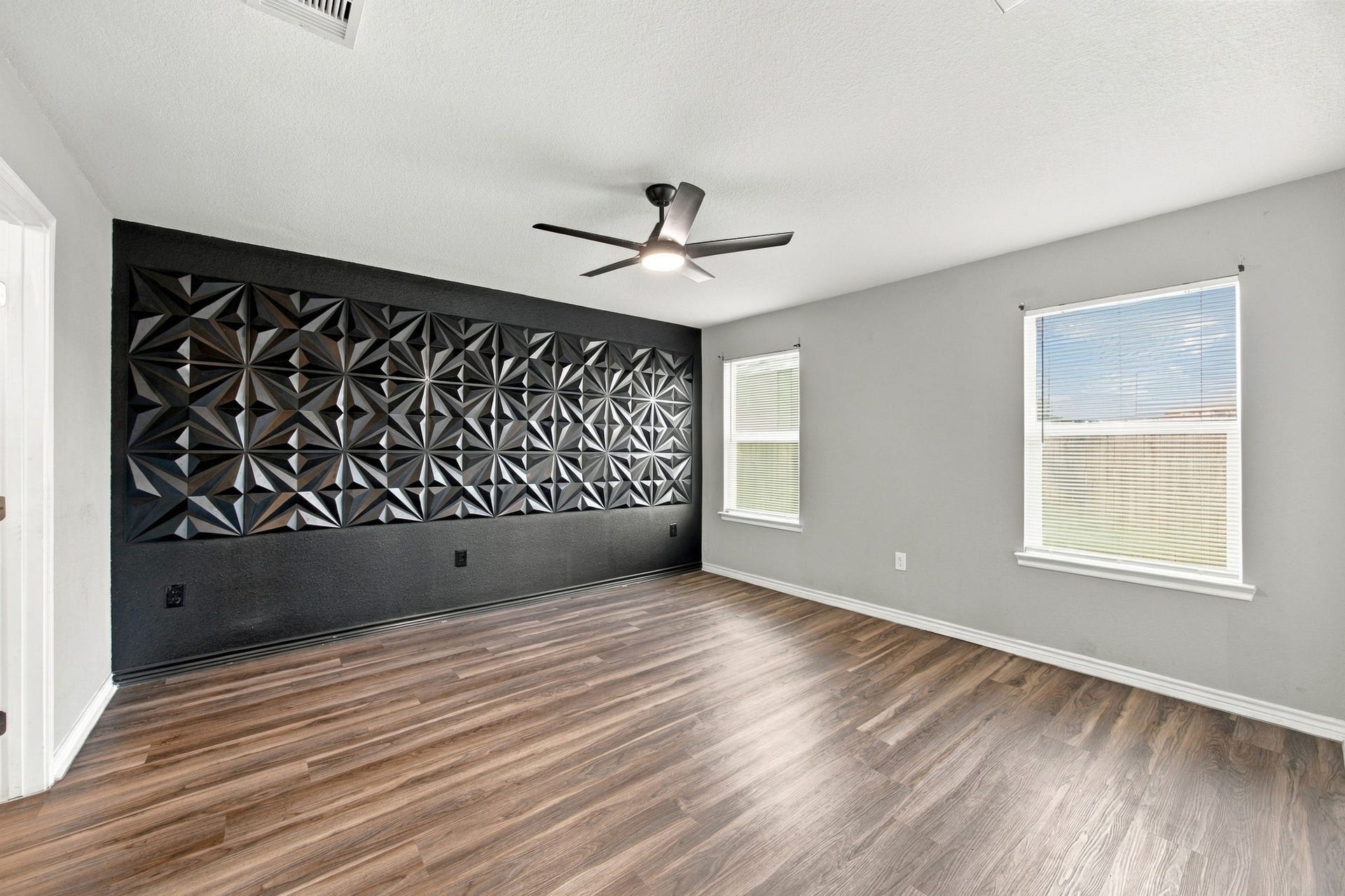 Bedroom featuring a striking geometric black accent wall, modern ceiling fan, wood-look flooring, and natural light.