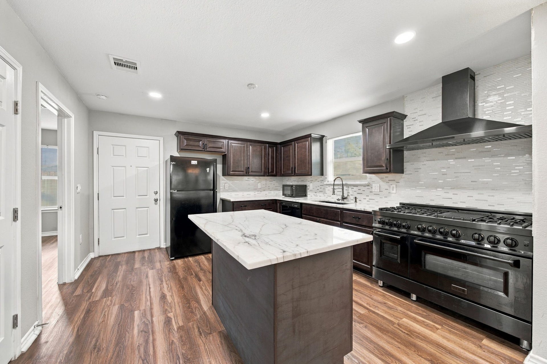Updated kitchen featuring dark cabinetry, marble-look countertops, a center island, and a large stainless-steel gas range.
