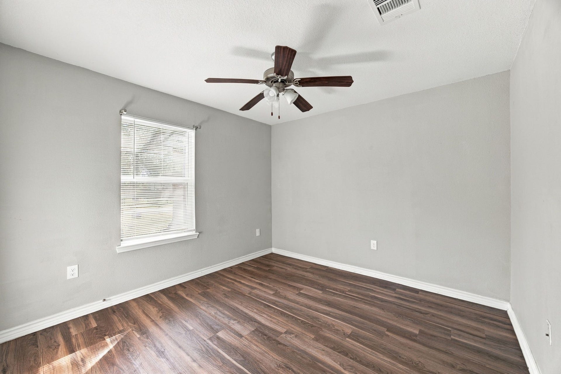 Bedroom featuring wood-look flooring, neutral gray walls, a ceiling fan, and natural light from the window.