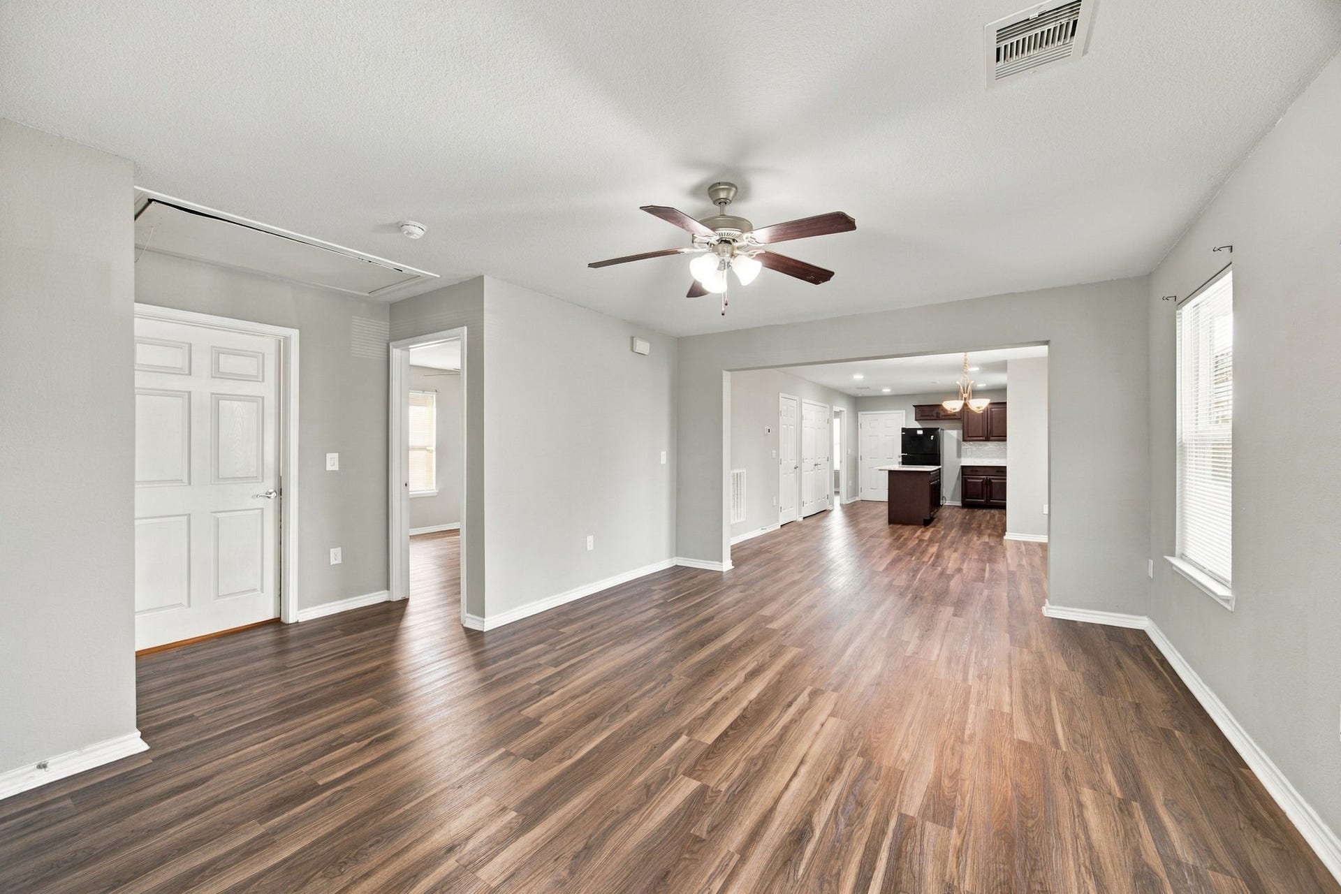Spacious living area featuring wood-look flooring, neutral walls, a ceiling fan, and an open connection to the kitchen.