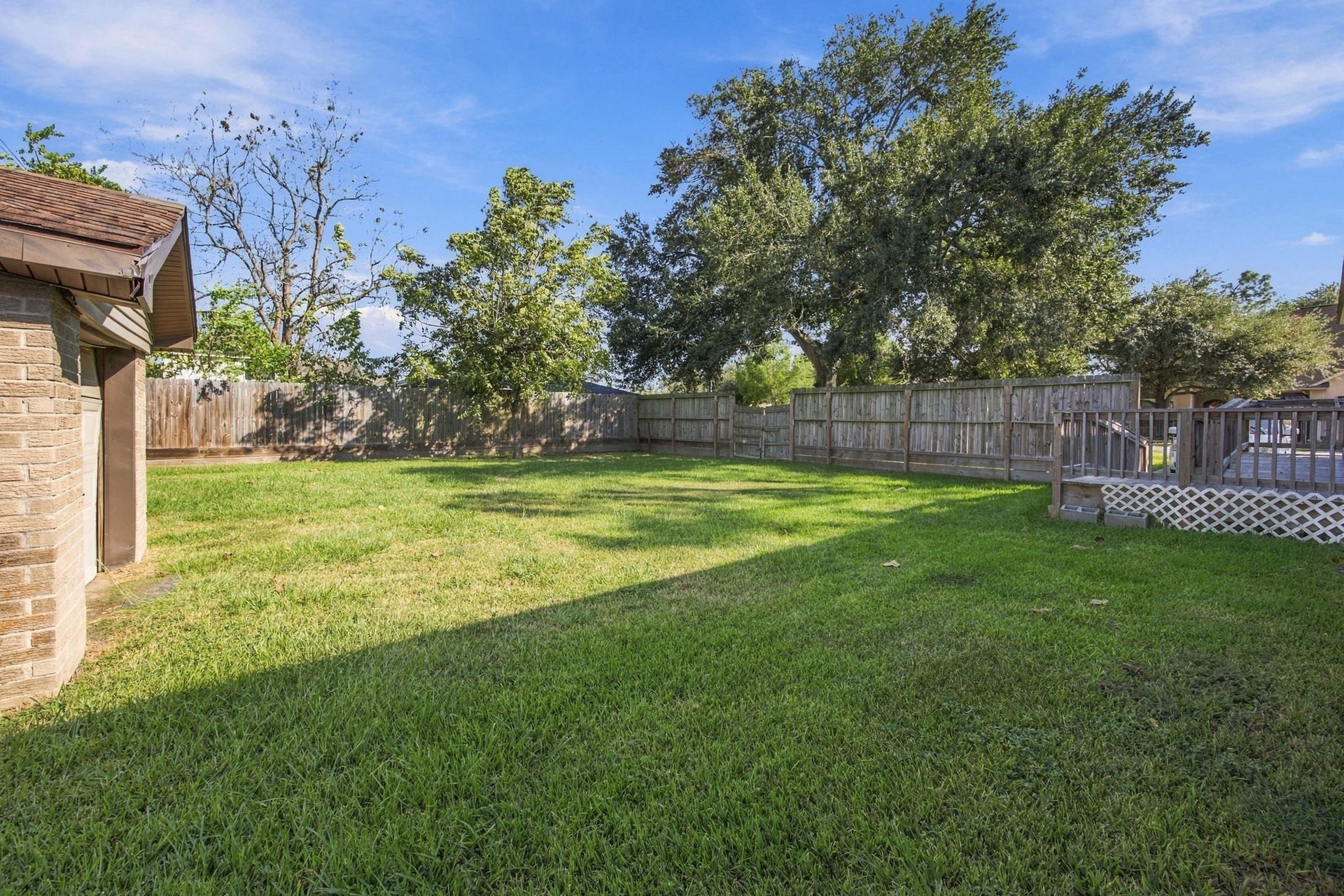 Large grassy backyard with mature trees, wood privacy fencing, and plenty of room for outdoor activities.