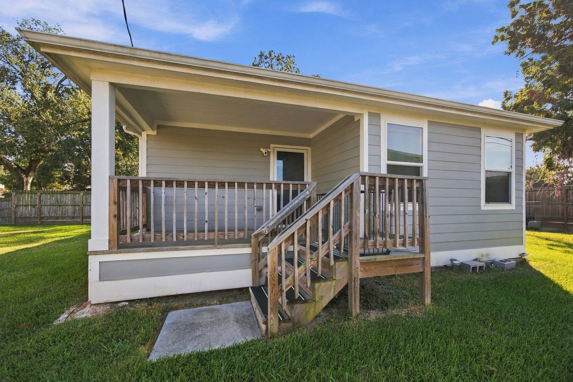 Back exterior view showcasing the covered porch, wooden stairs, fenced yard, and inviting outdoor space.