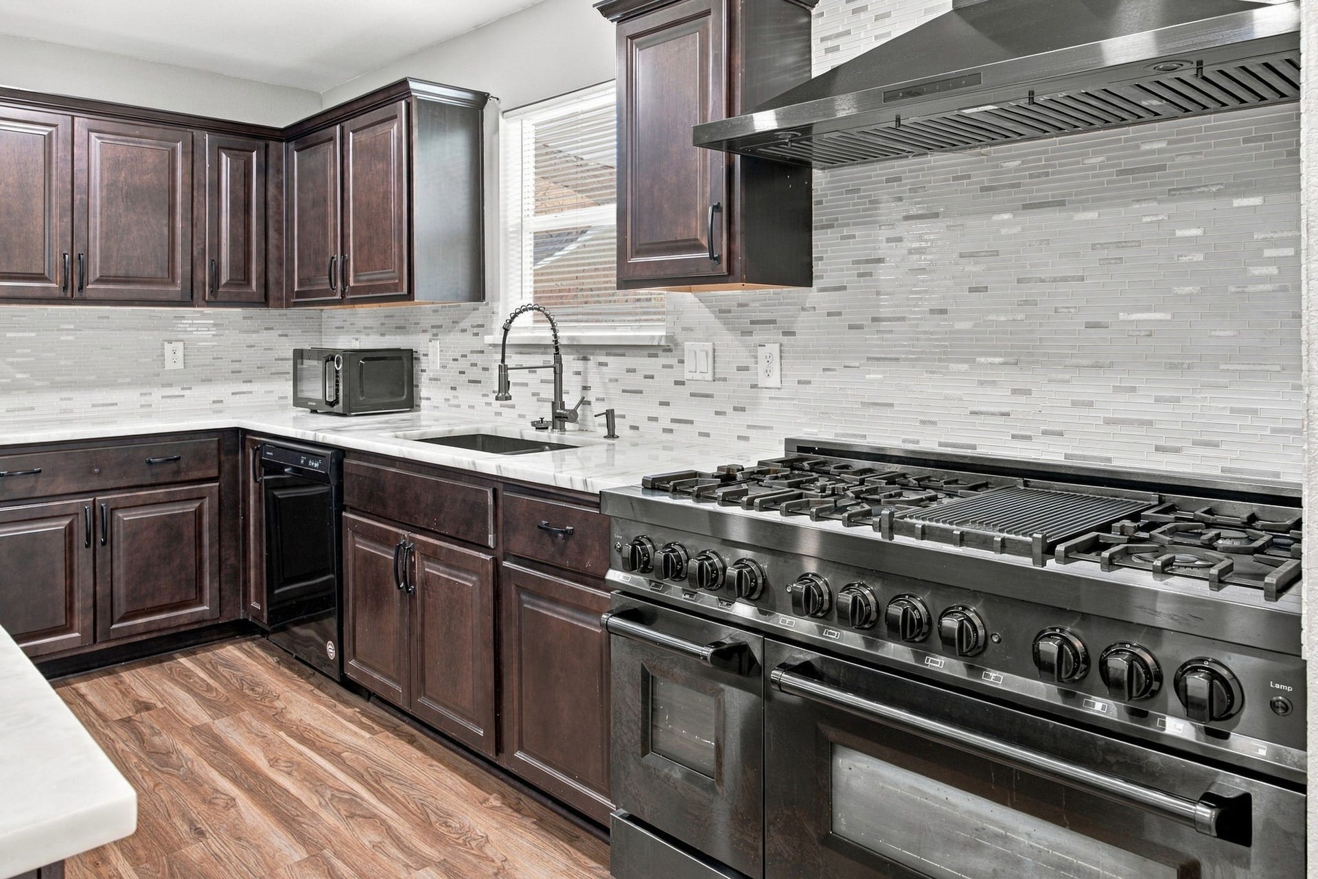 Updated kitchen featuring dark cabinetry, marble-look countertops, a center island, and a large stainless-steel gas range.