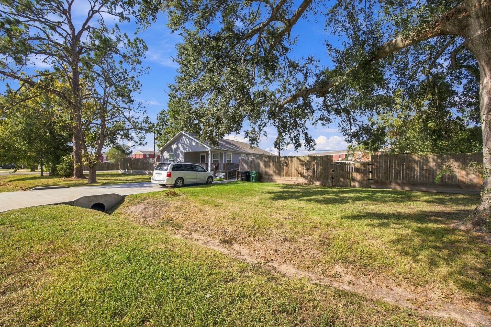 Wide view of the property featuring a spacious grassy yard, mature trees, and surrounding privacy fencing.