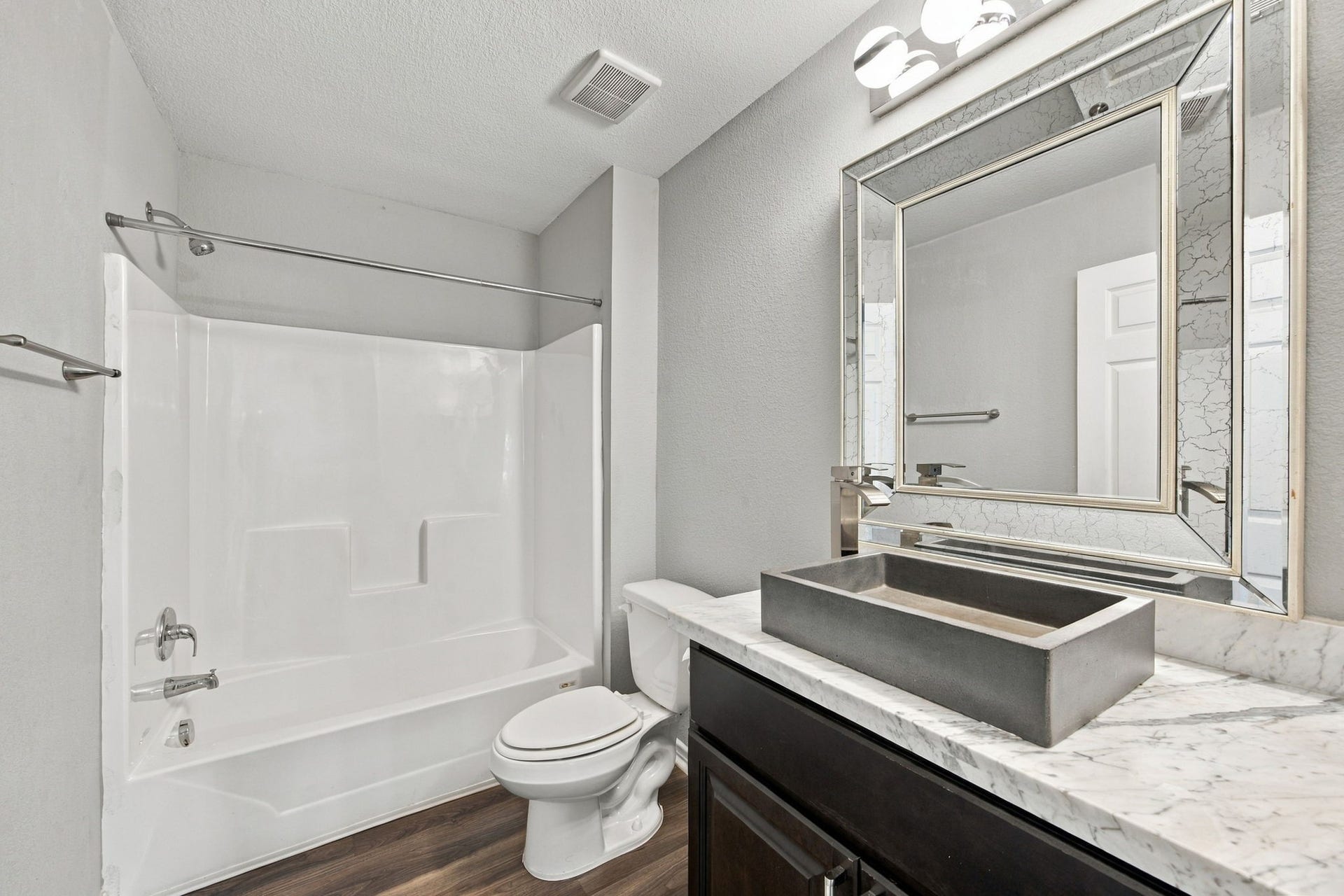 Updated bathroom showcasing a bathtub and shower combination, marble-look vanity countertop, modern vessel sink, and framed mirror.