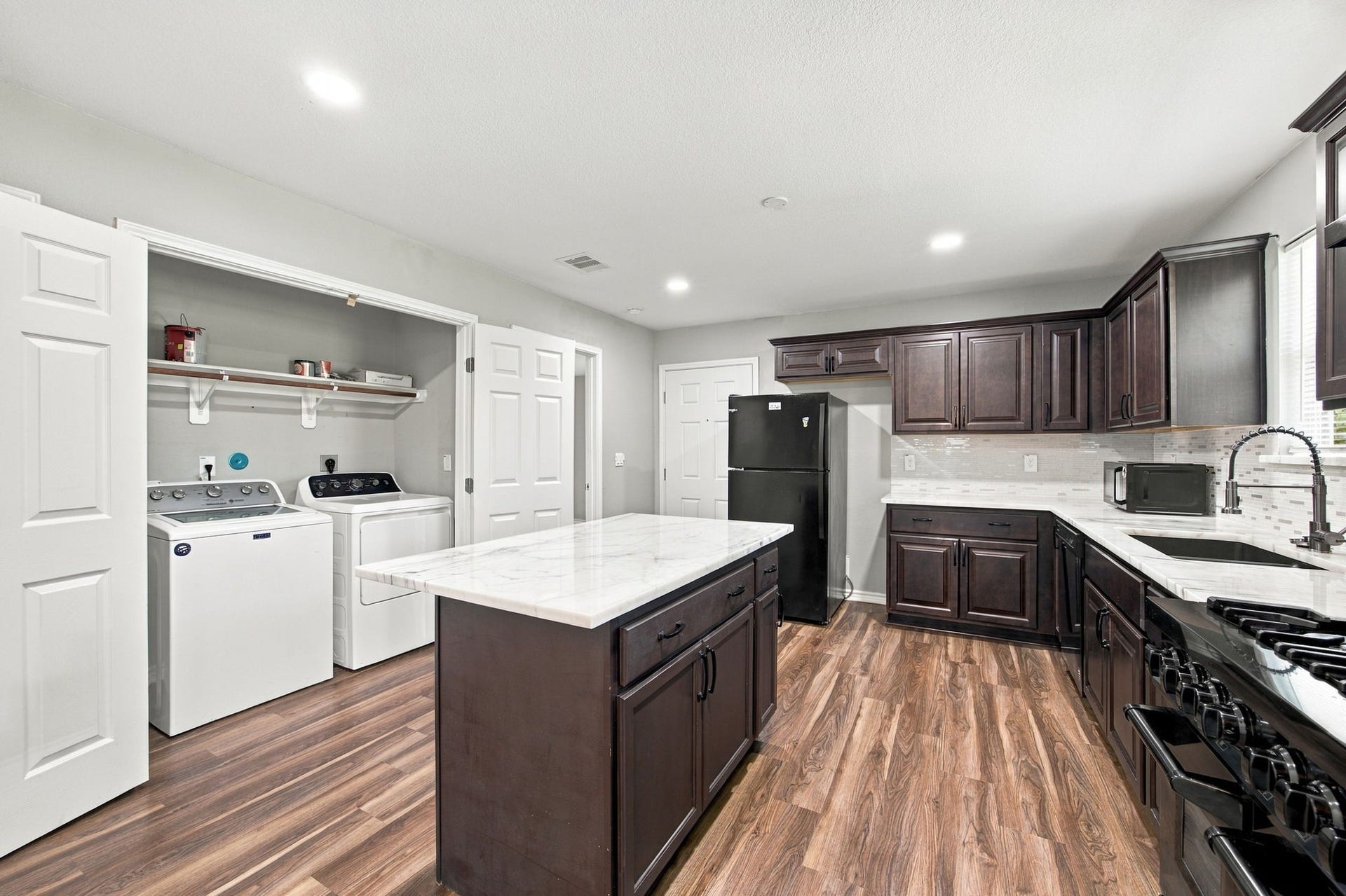 Spacious kitchen with a center island, marble-look countertops, dark cabinetry, gas range, and a convenient in-kitchen laundry area.