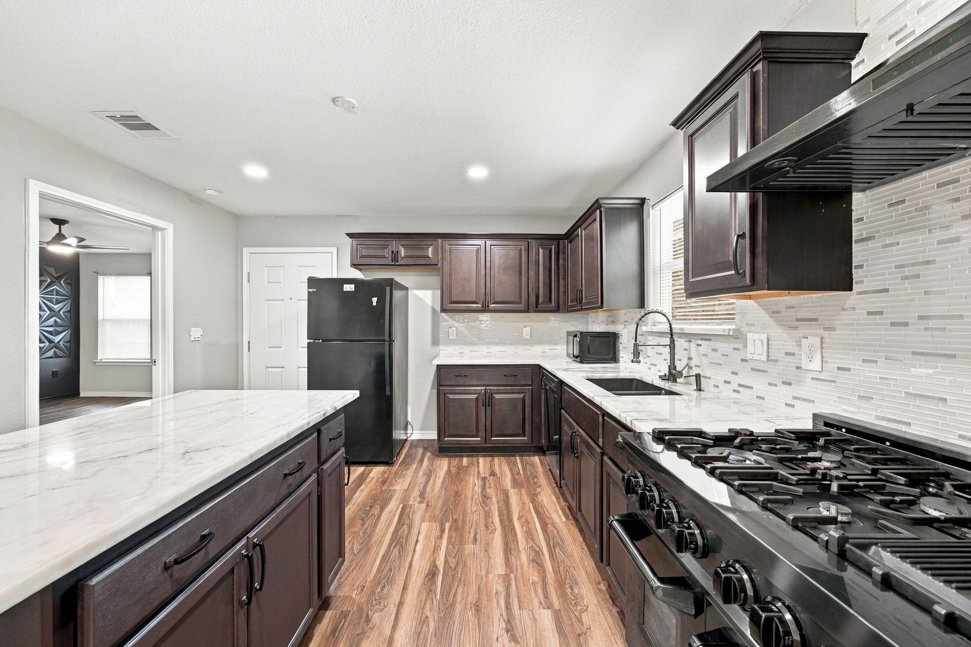Updated kitchen featuring dark wood cabinetry, marble-look countertops, a spacious island, stainless steel sink, gas range, and modern tile backsplash.