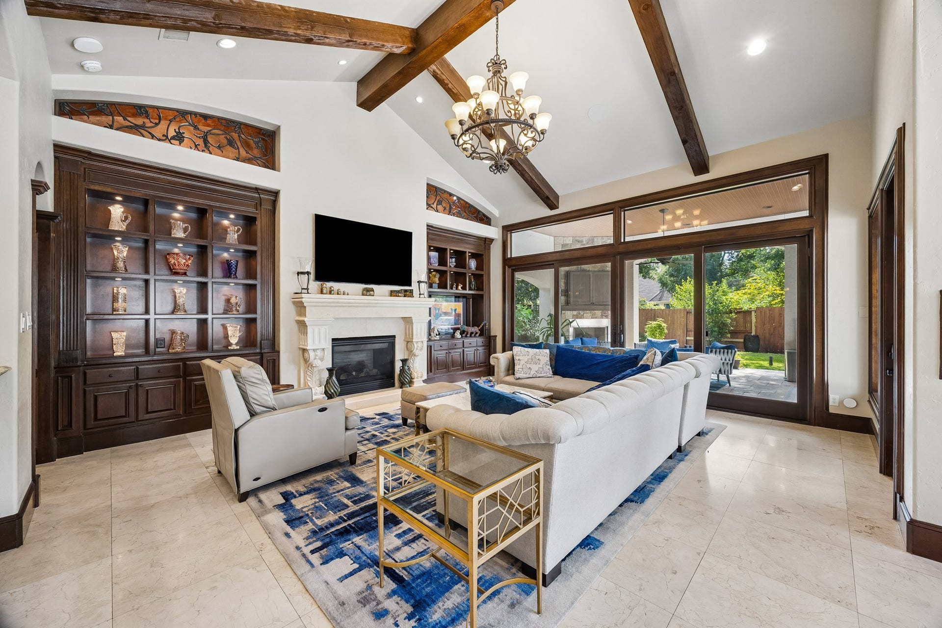 8111 Marshall Falls Drive, Spring, TX 77379 Spacious family room with elegant wooden beams, a grand fireplace, and large windows offering a view of the lush backyard. There is a covered patio with a fireplace and summer kitchen just off the family room.