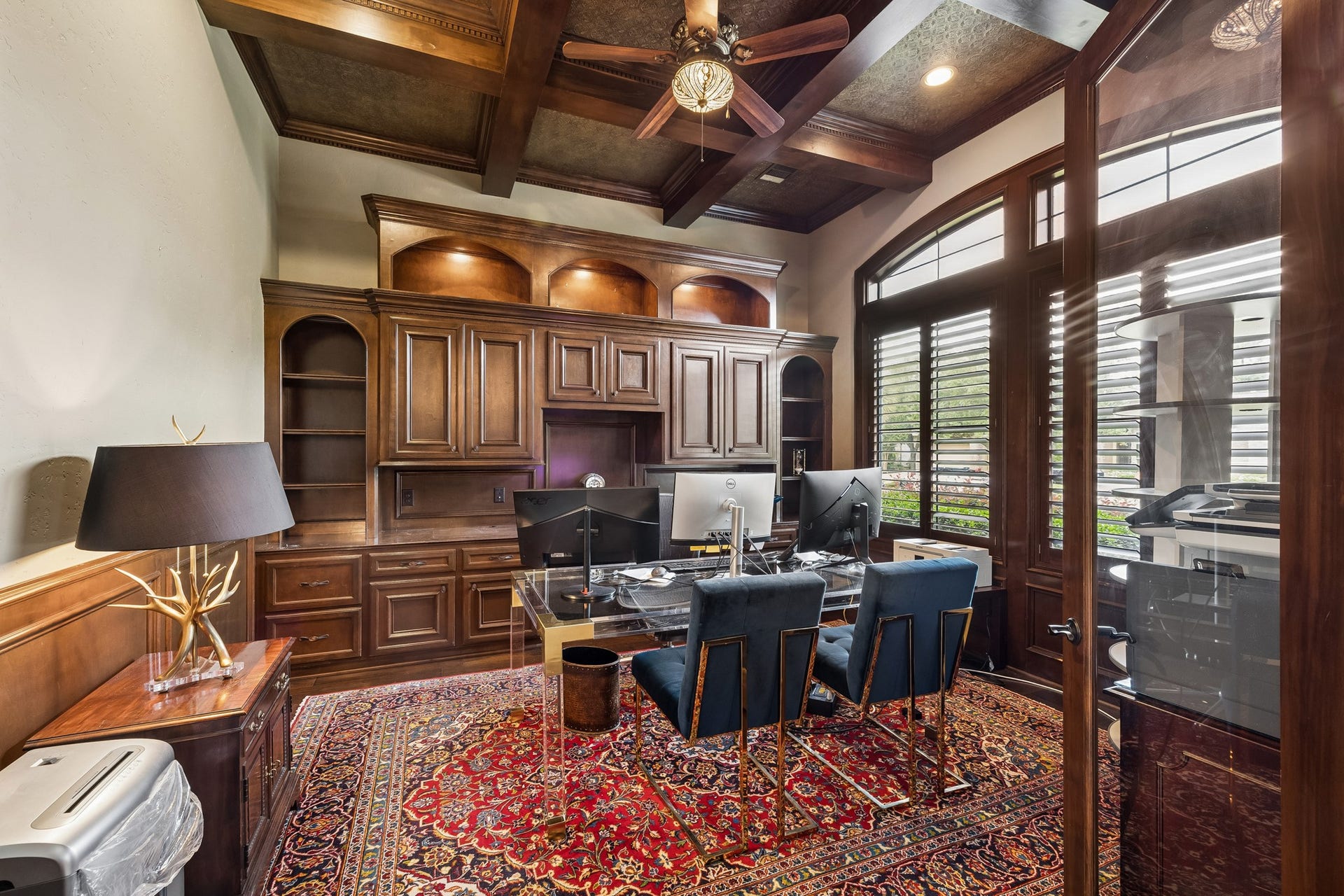 8111 Marshall Falls Drive, Spring, TX 77379 Elegant library featuring rich wood cabinetry, a coffered ceiling, and large windows with plantation shutters.