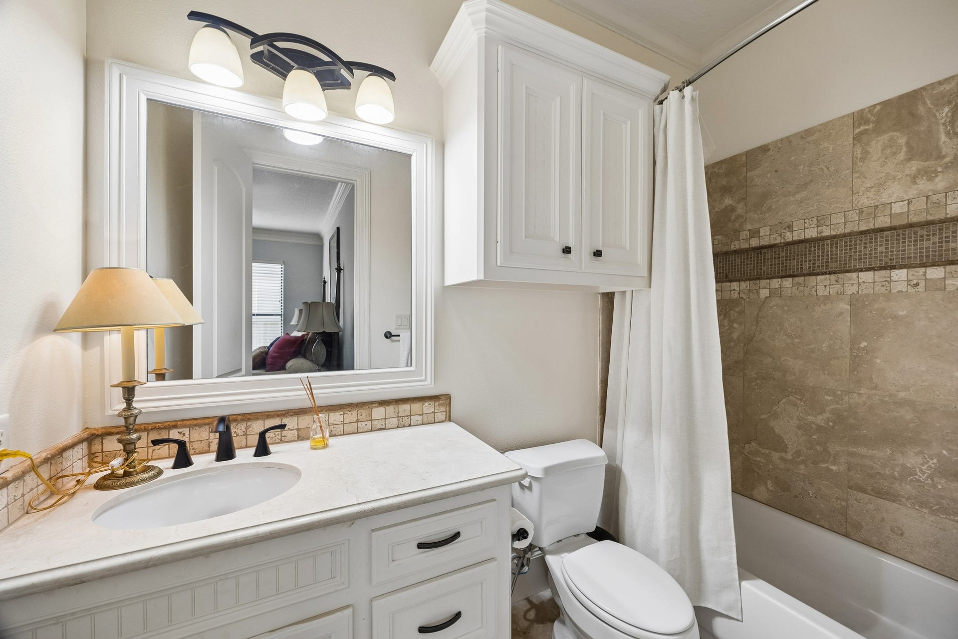 8111 Marshall Falls Drive, Spring, TX 77379 Charming en-suite bathroom featuring a sleek vanity with a marble countertop, elegant lighting, and a tiled shower with a classic curtain for a timeless look.